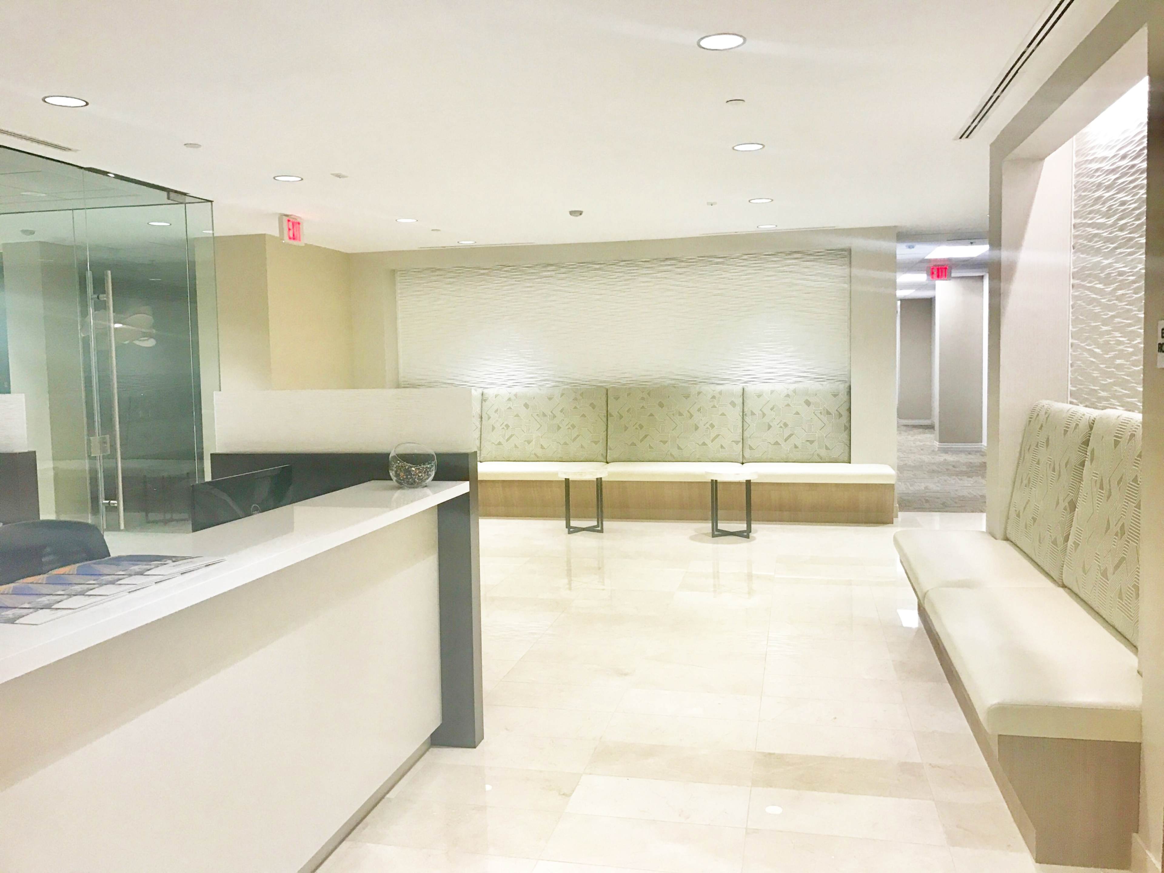 The image shows a modern reception area with a reception desk, seating benches, and a textured wall in a well-lit space.