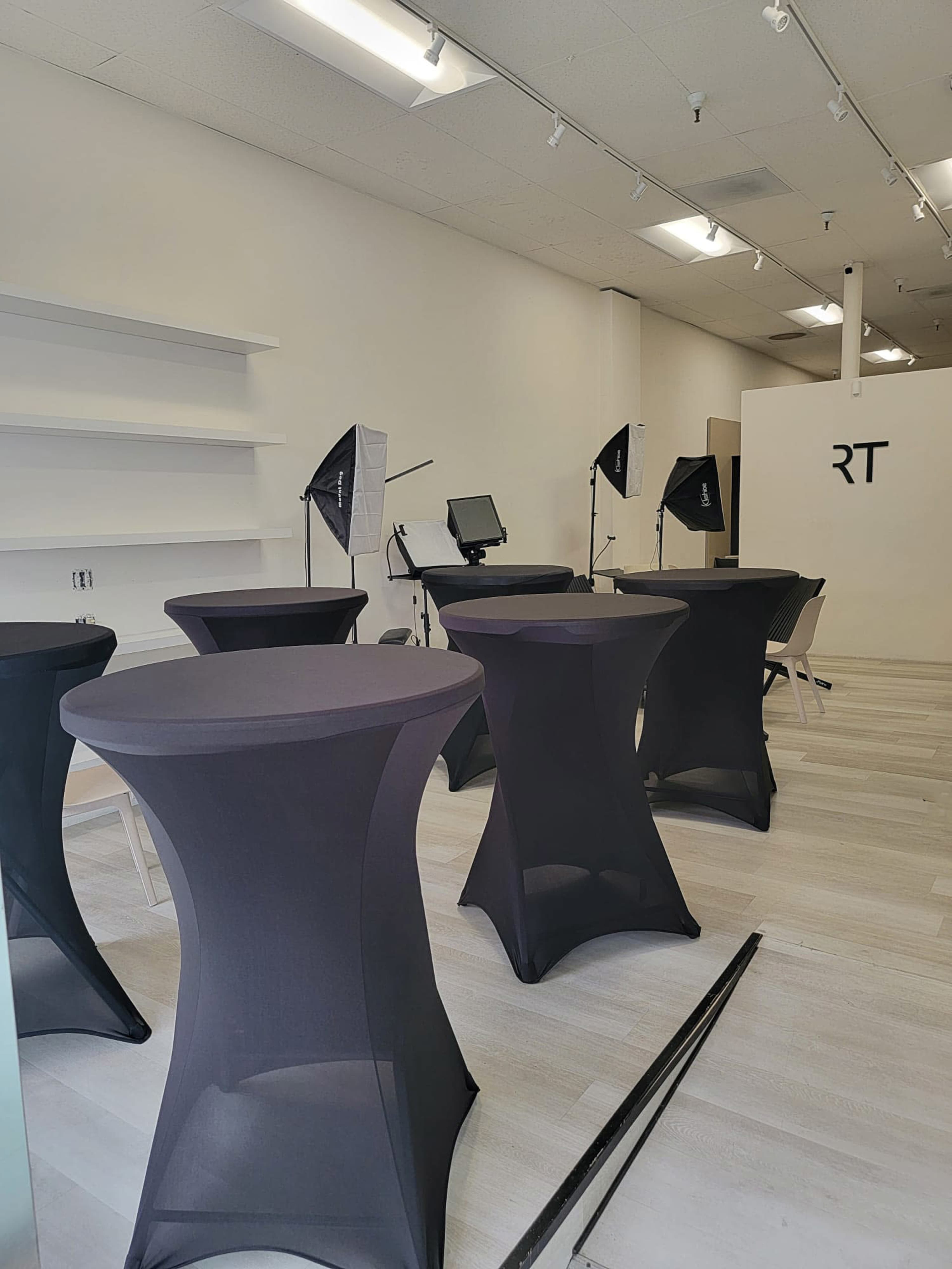 The image shows a spacious room with several black cocktail tables and photography lighting setups in the background.