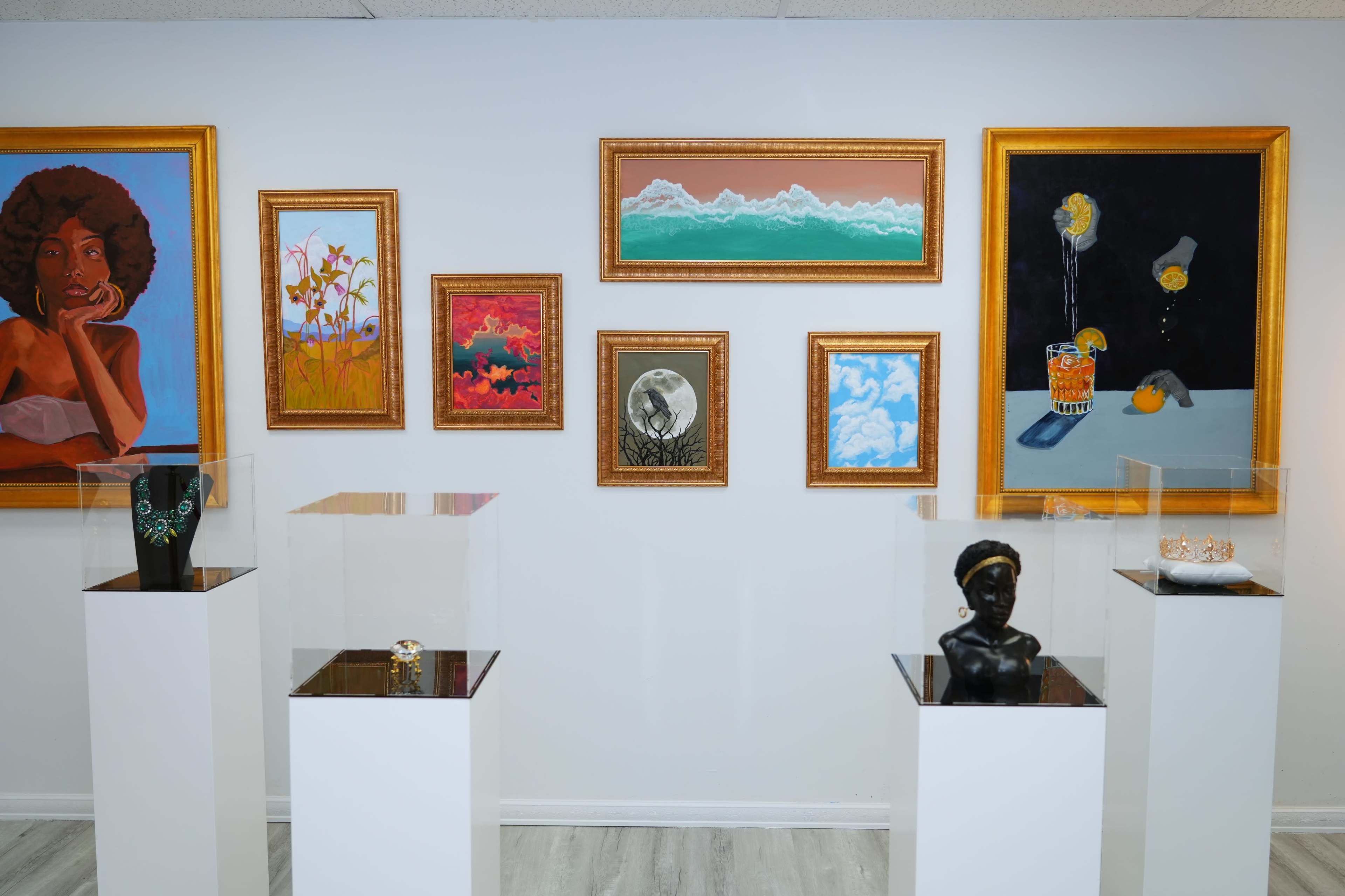 An art gallery featuring various framed paintings and sculptures displayed on white pedestals.