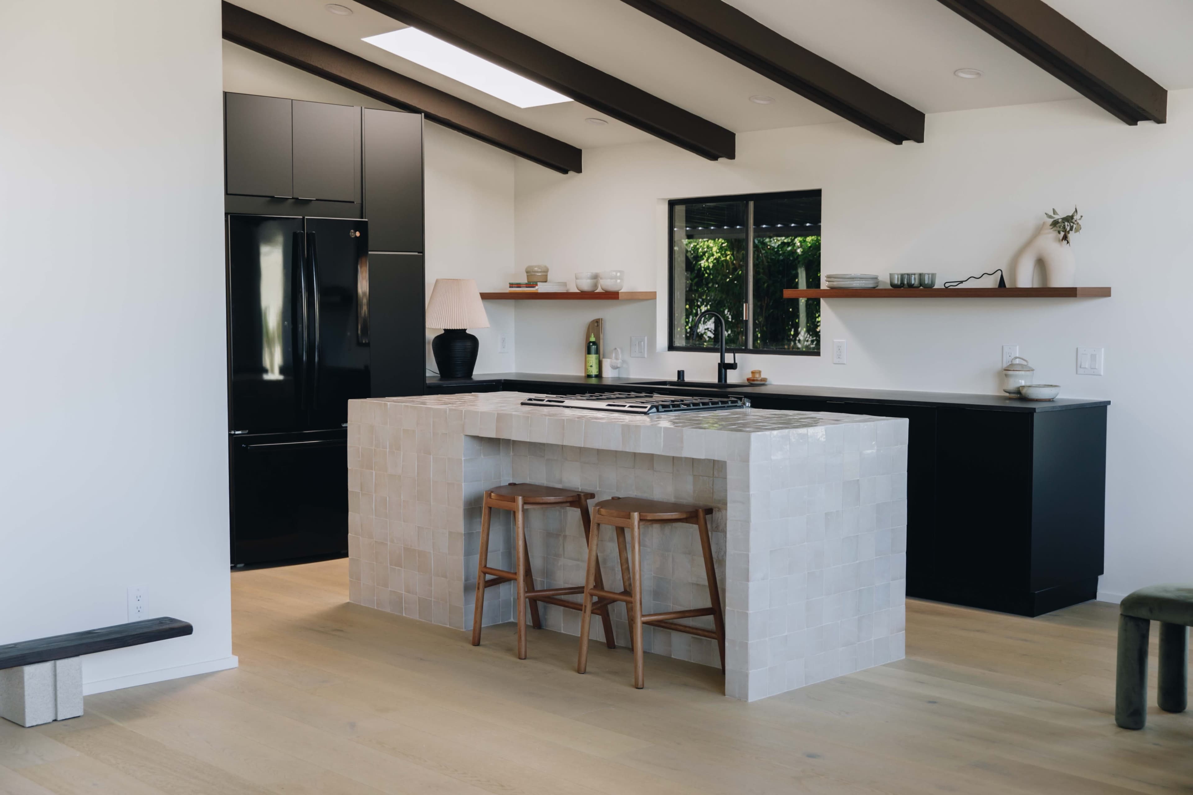A modern kitchen features a central island with a stovetop, black appliances, and light wood flooring.