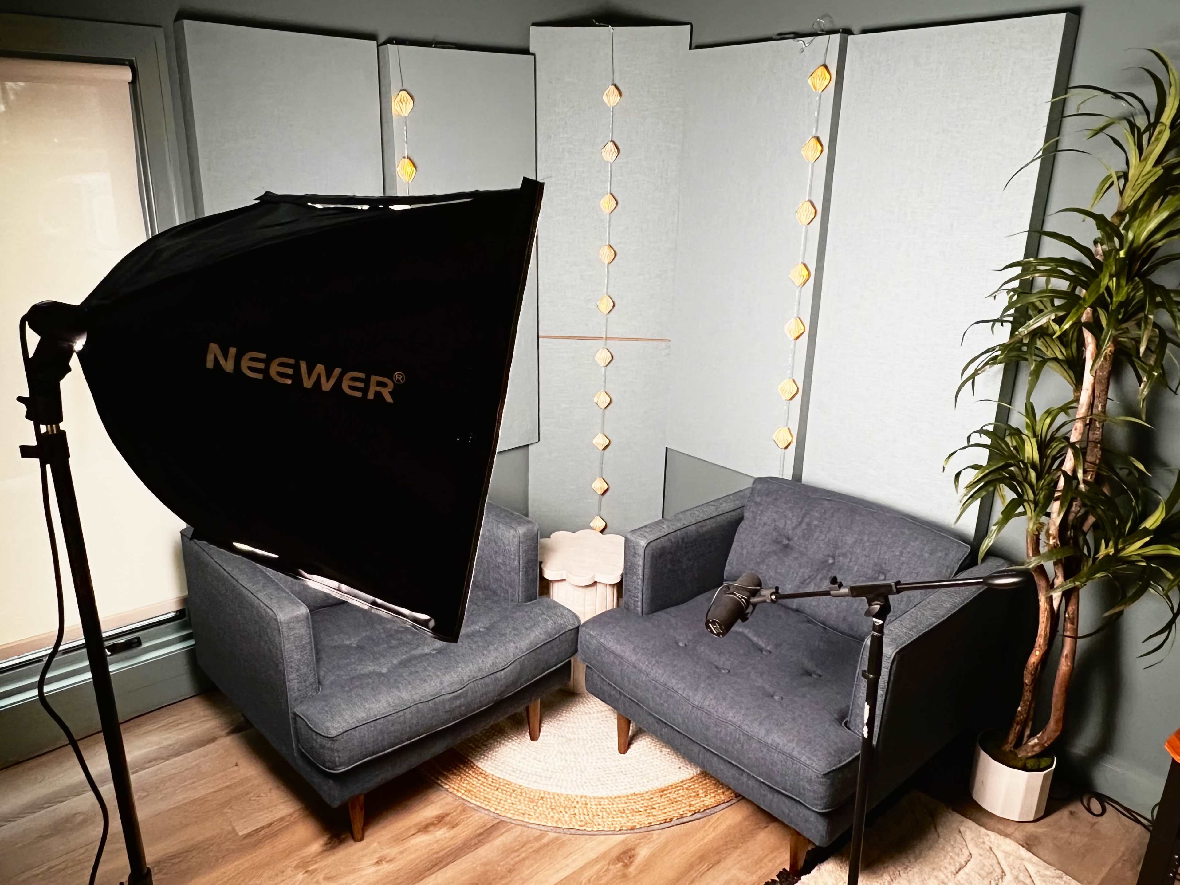 The image shows a well-lit room with two blue armchairs, a small white table, a microphone on a stand, and decorative lights hanging in the background.