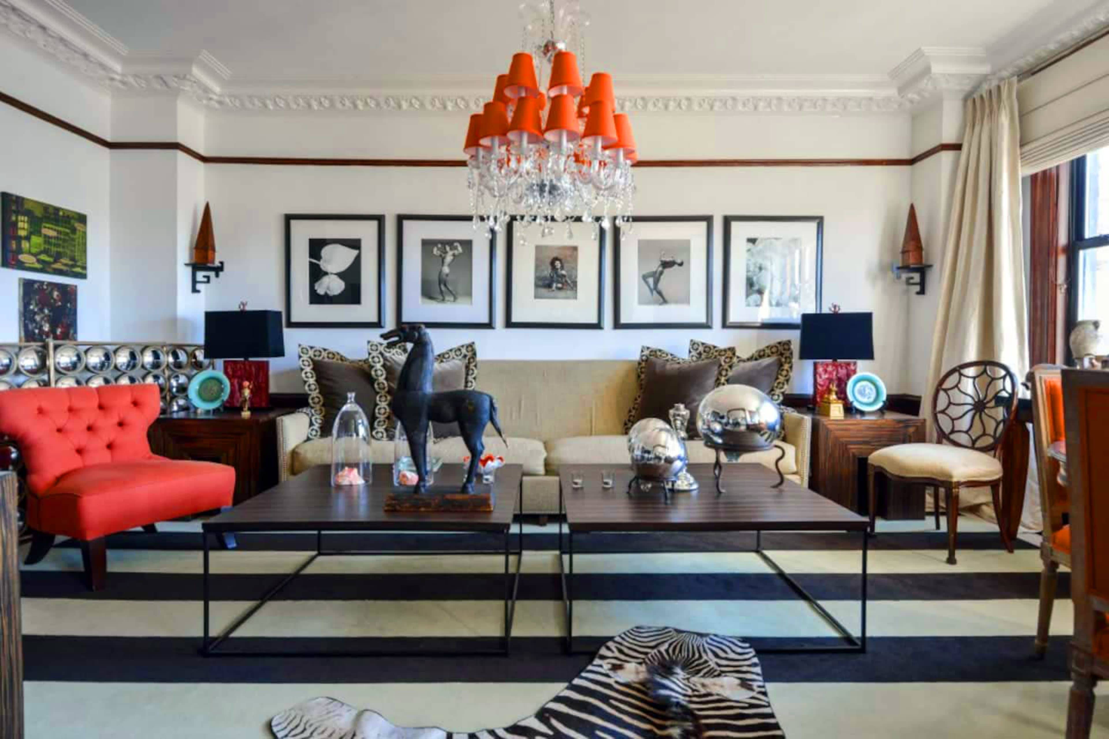 The living room features a mix of modern and eclectic furniture, including a red sofa, patterned cushions, and a variety of decorative objects arranged around a central coffee table.