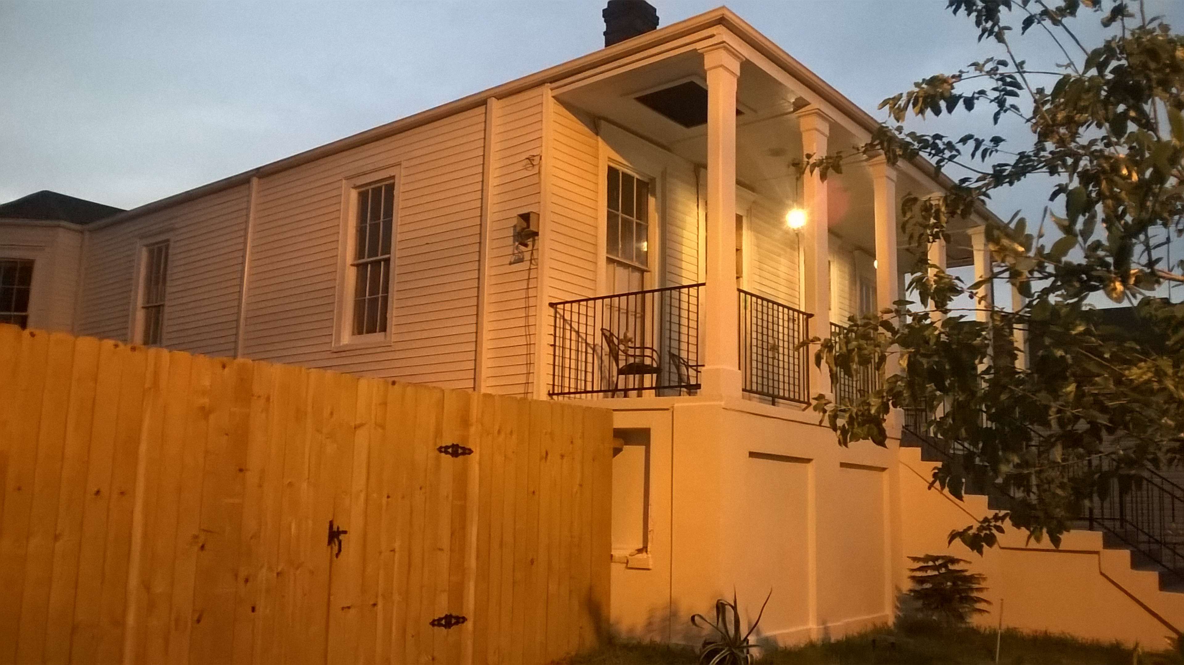 A two-story house with a front porch and a wooden fence surrounds the property, illuminated by an evening glow.