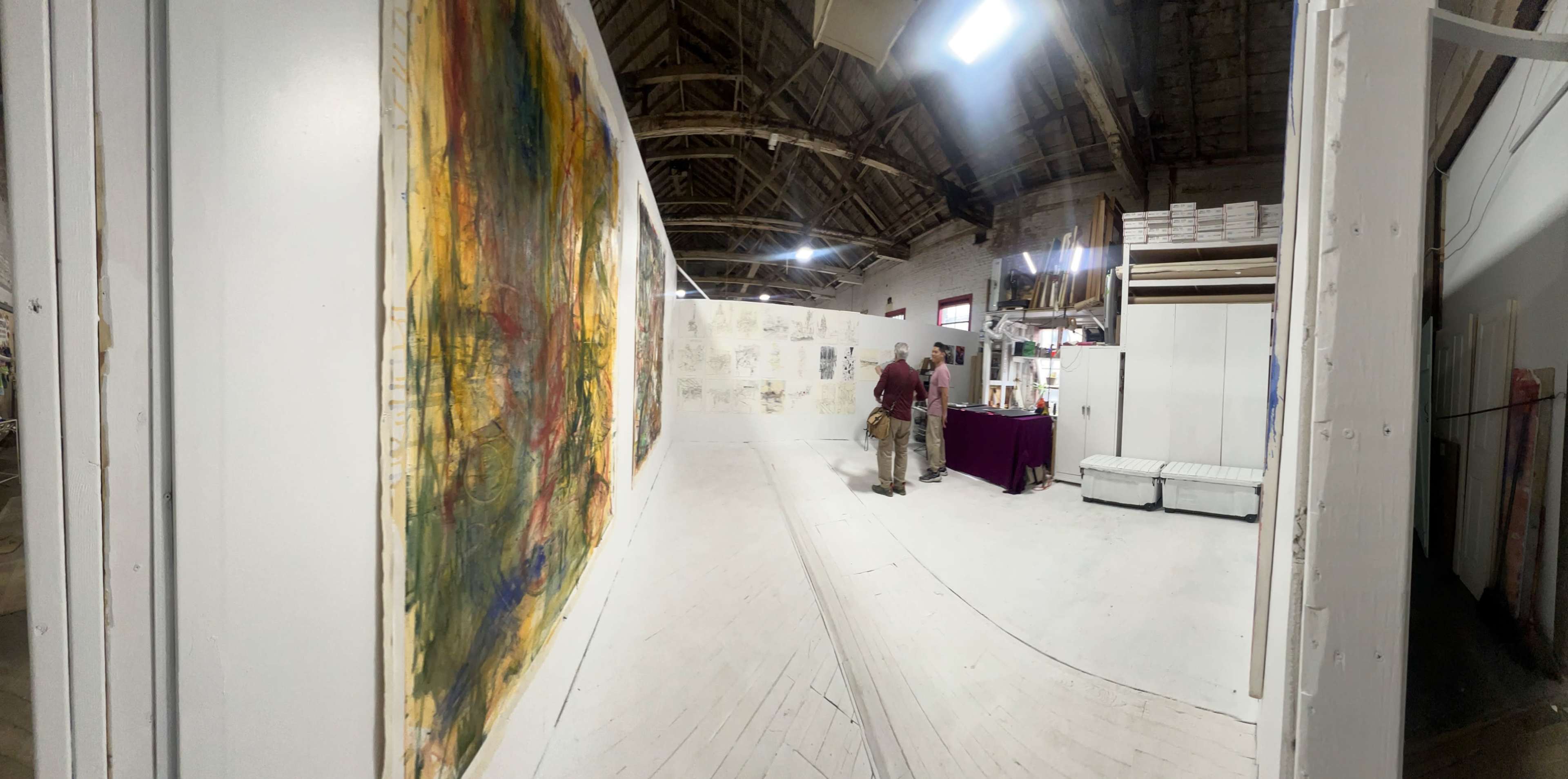 An artist is positioned near a large abstract painting in a spacious gallery with exposed wooden beams.