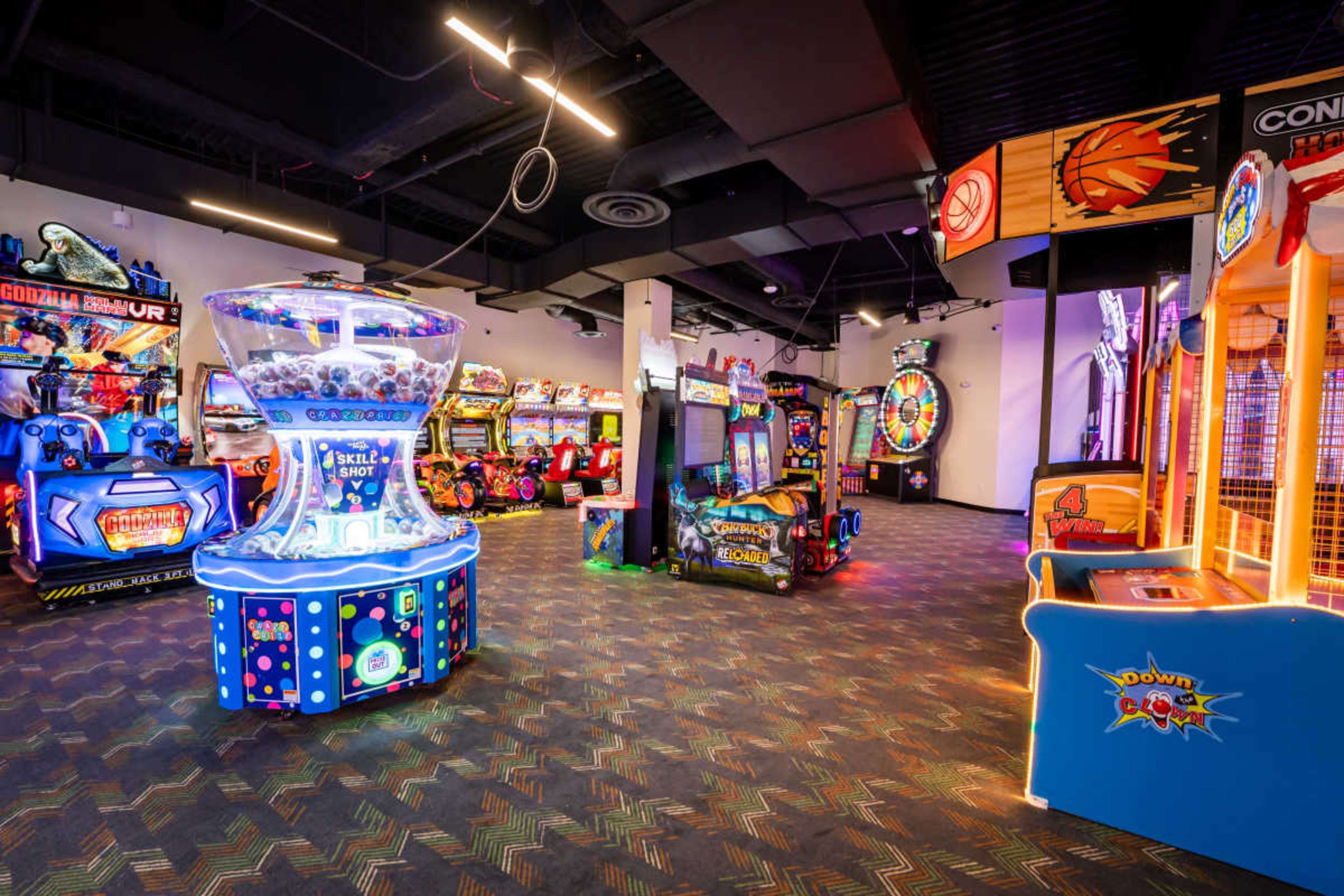 The image shows an arcade filled with various colorful gaming machines and equipment arranged in a spacious room.