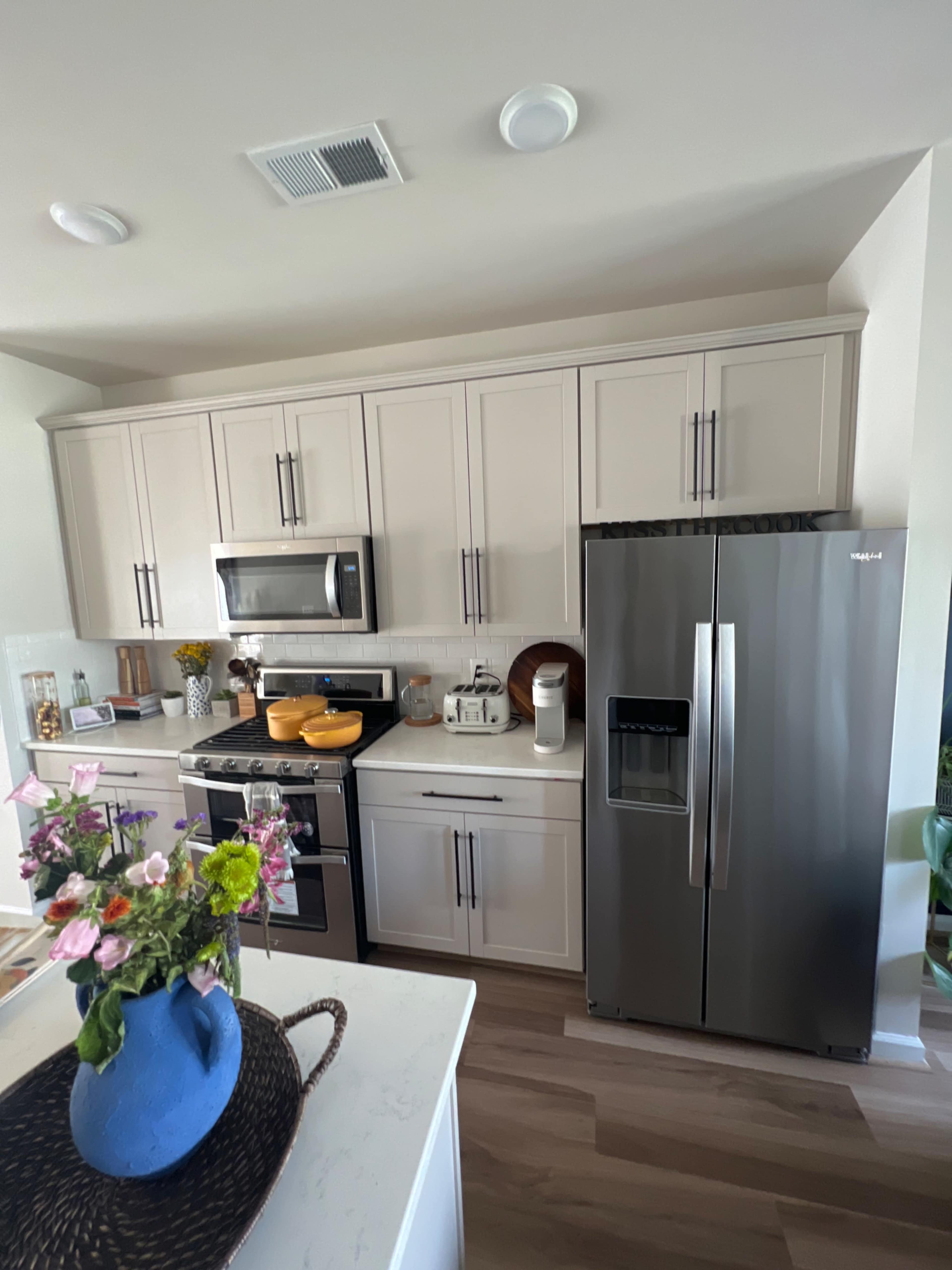 The kitchen features modern cabinetry, stainless steel appliances, and a countertop with decorative items and a blue vase containing flowers.
