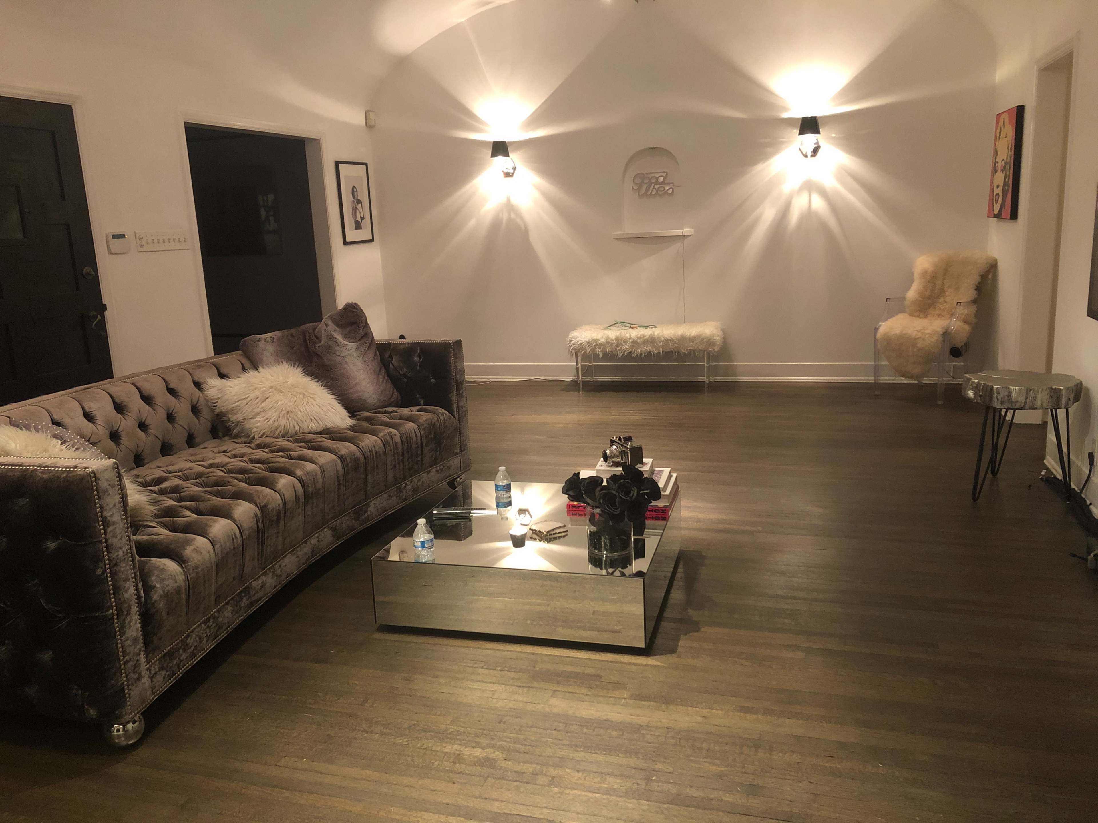 A modern living room with a tufted velvet sofa, a glass coffee table, and stylish light fixtures illuminating the space.