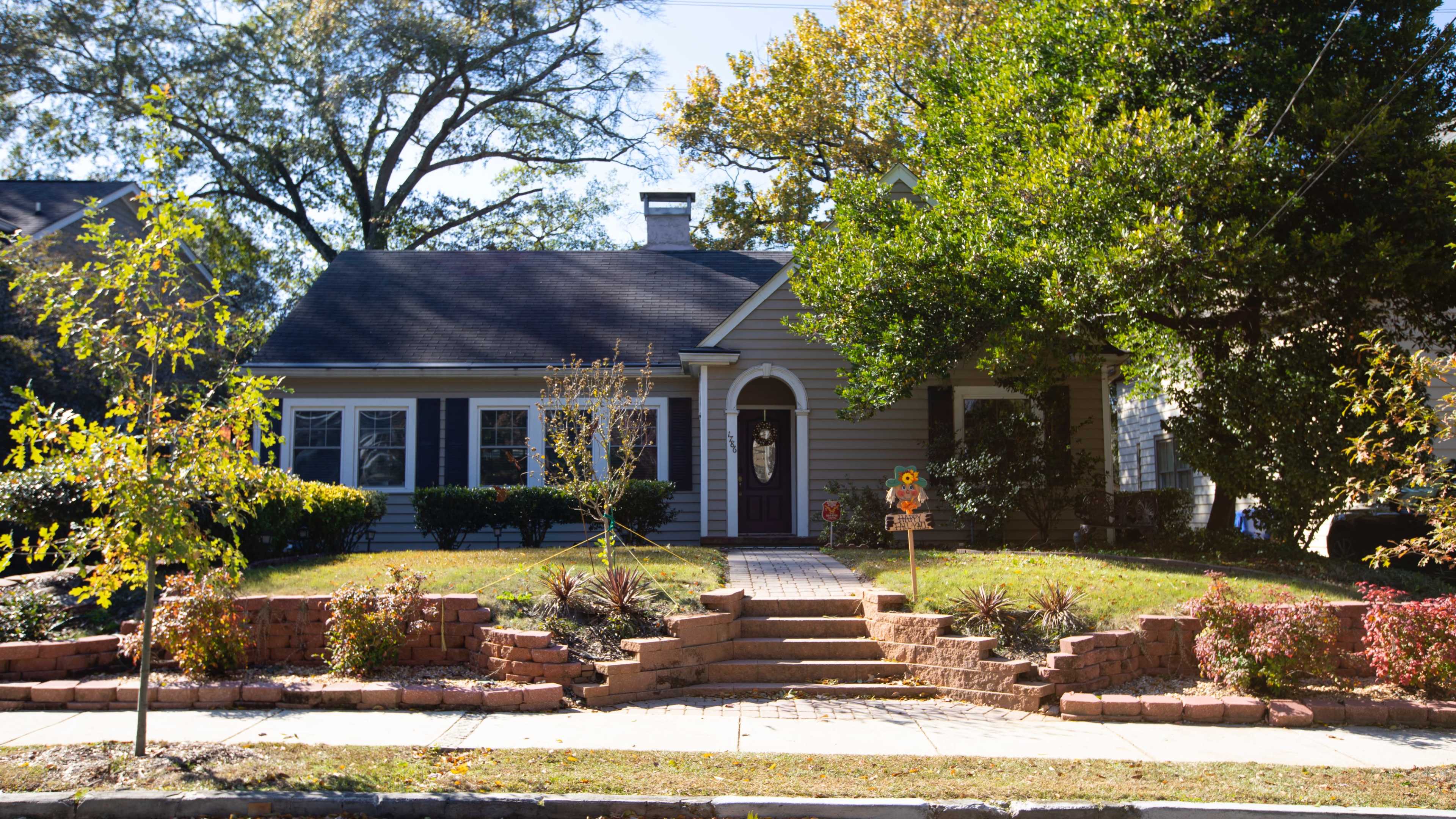 A single-story, gray house with a purple door features a landscaped front yard and a brick pathway leading to the entrance.