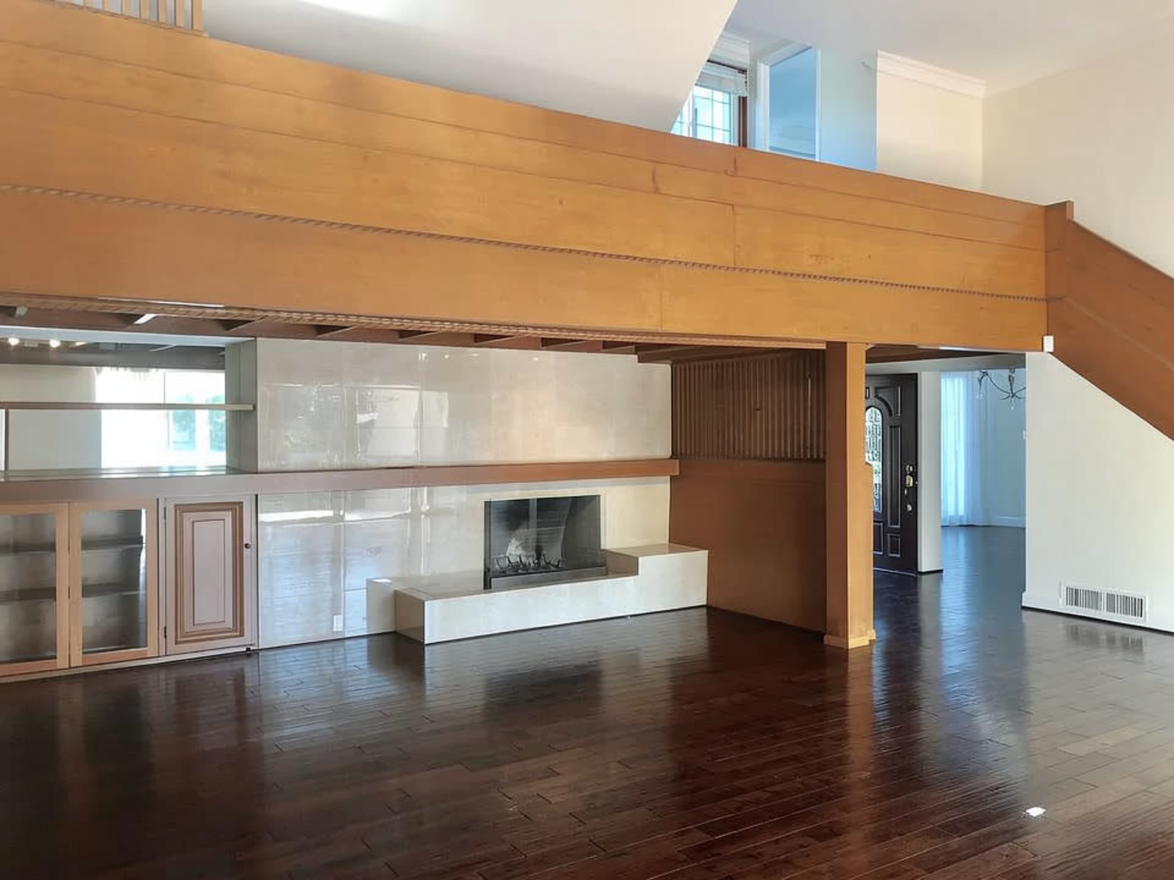The image shows a spacious interior with wooden flooring, a two-level design featuring a lofted area, and a modern fireplace surrounded by a sleek white wall.