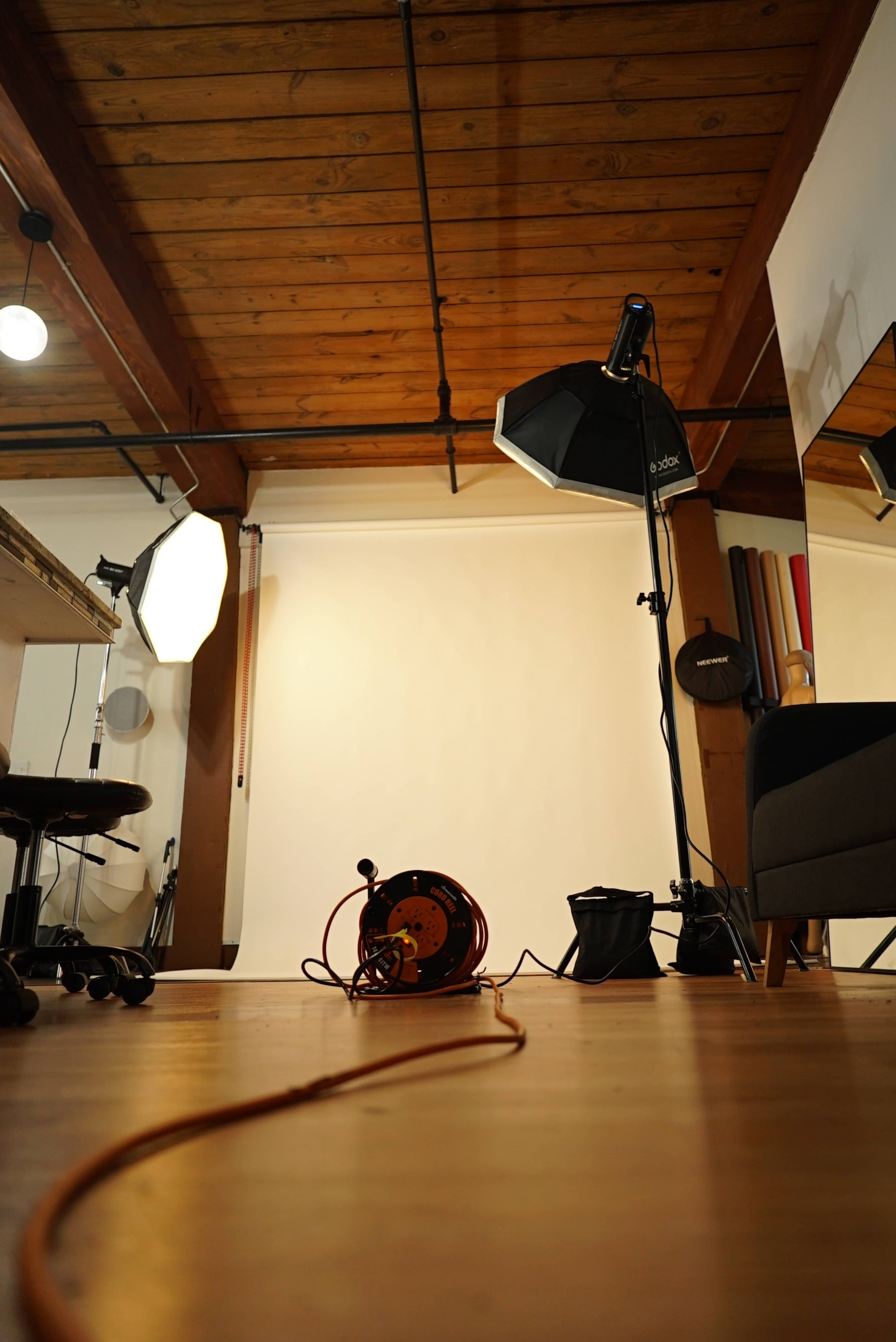The image shows a photography studio with softbox lights, a cabled extension reel on the floor, and a plain backdrop.