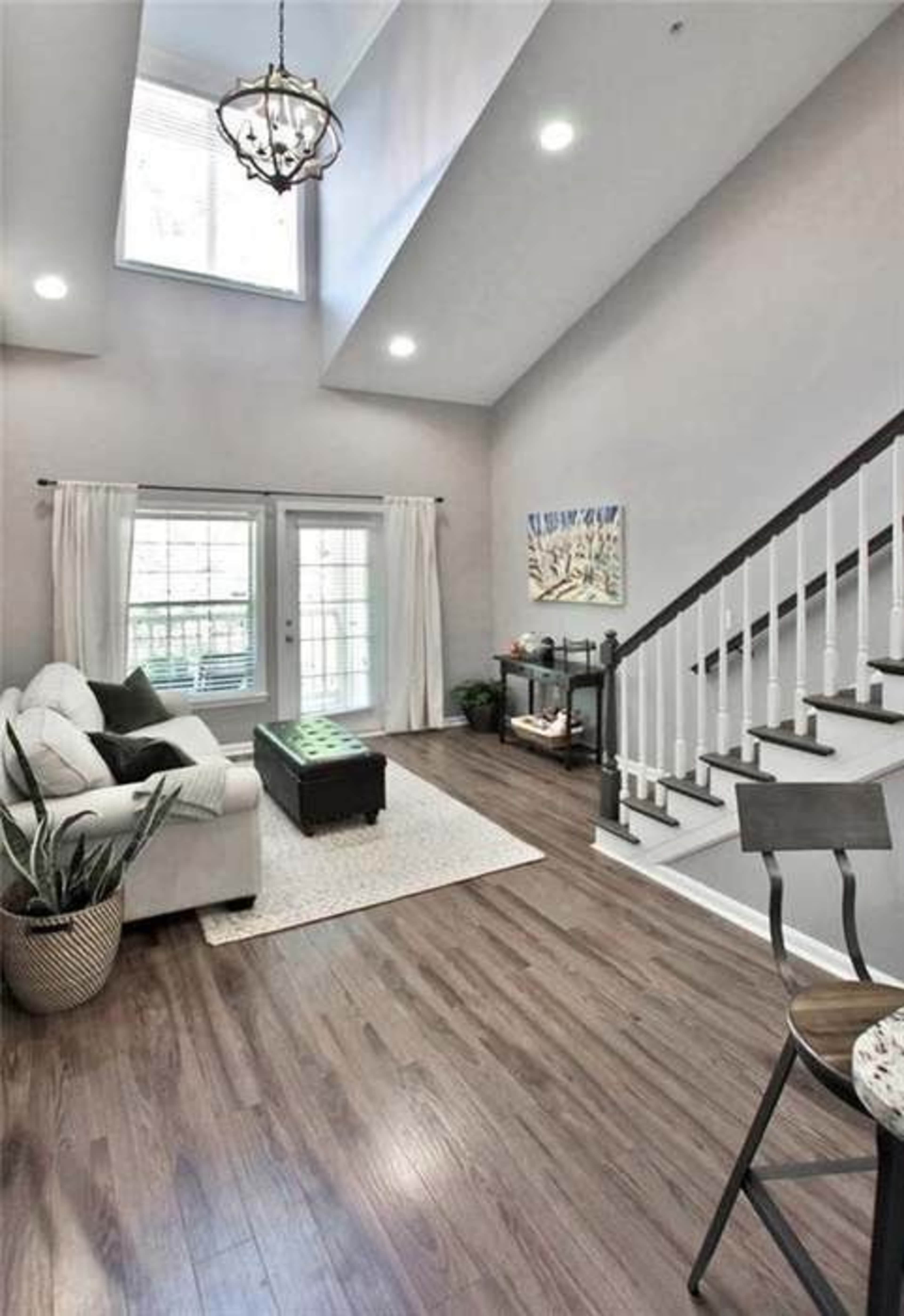 A bright living room features a white sofa, a coffee table, and a staircase leading to a balcony.