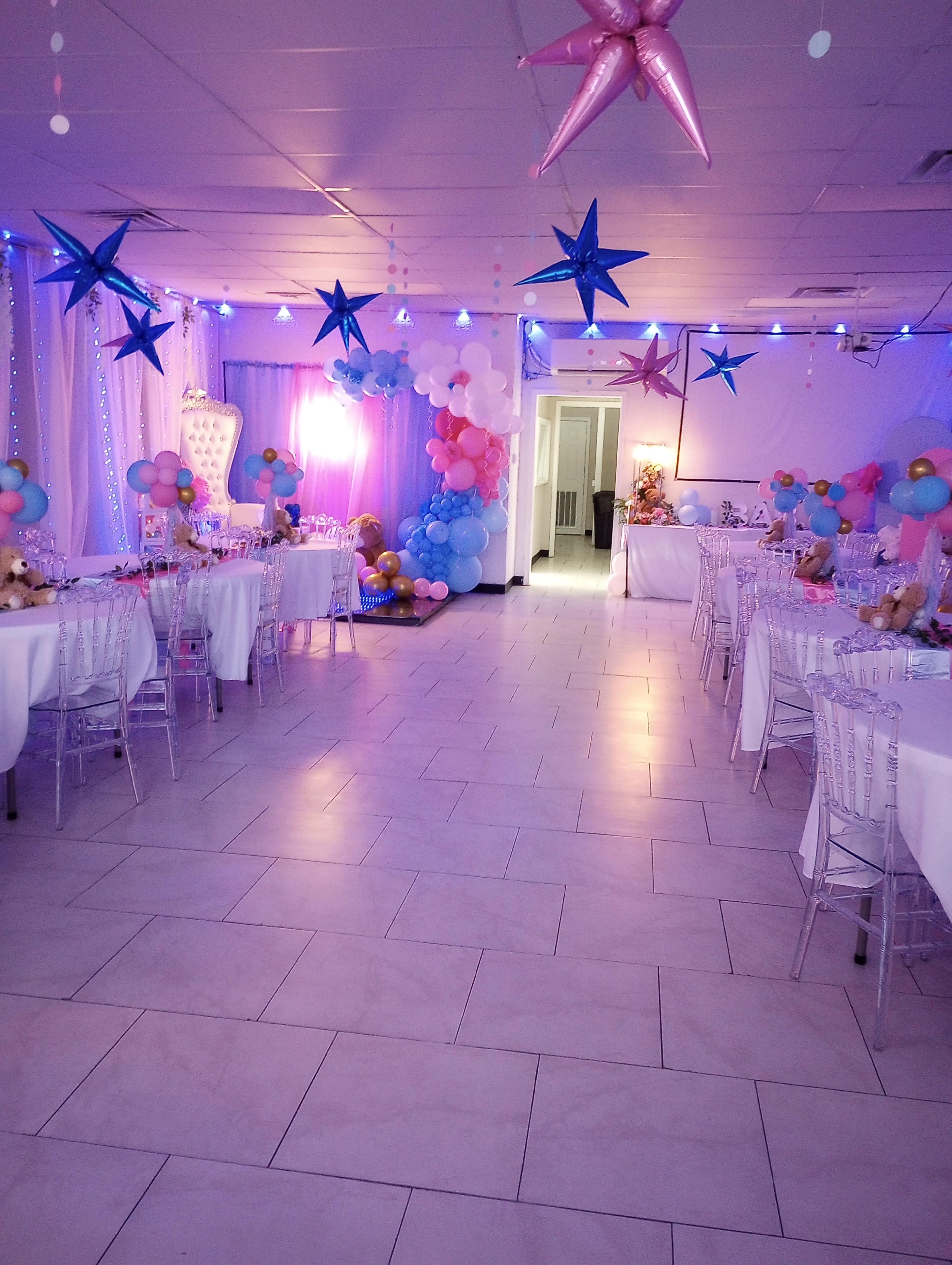 The image shows a decorated event space with tables set for a celebration, featuring colorful balloons, stars, and ambient lighting.