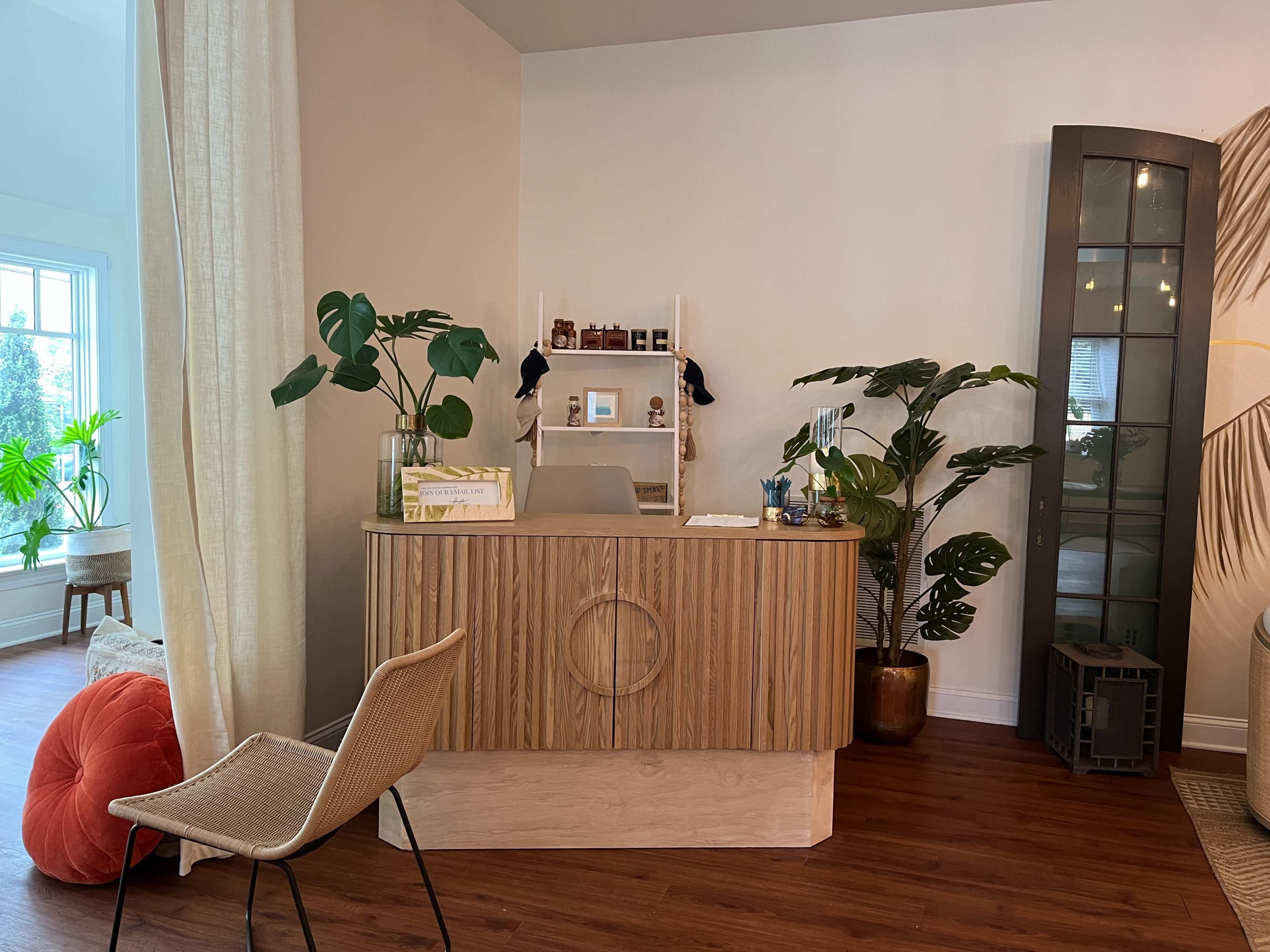 The image shows a modern reception area featuring a wooden front desk, indoor plants, and a comfortable chair.