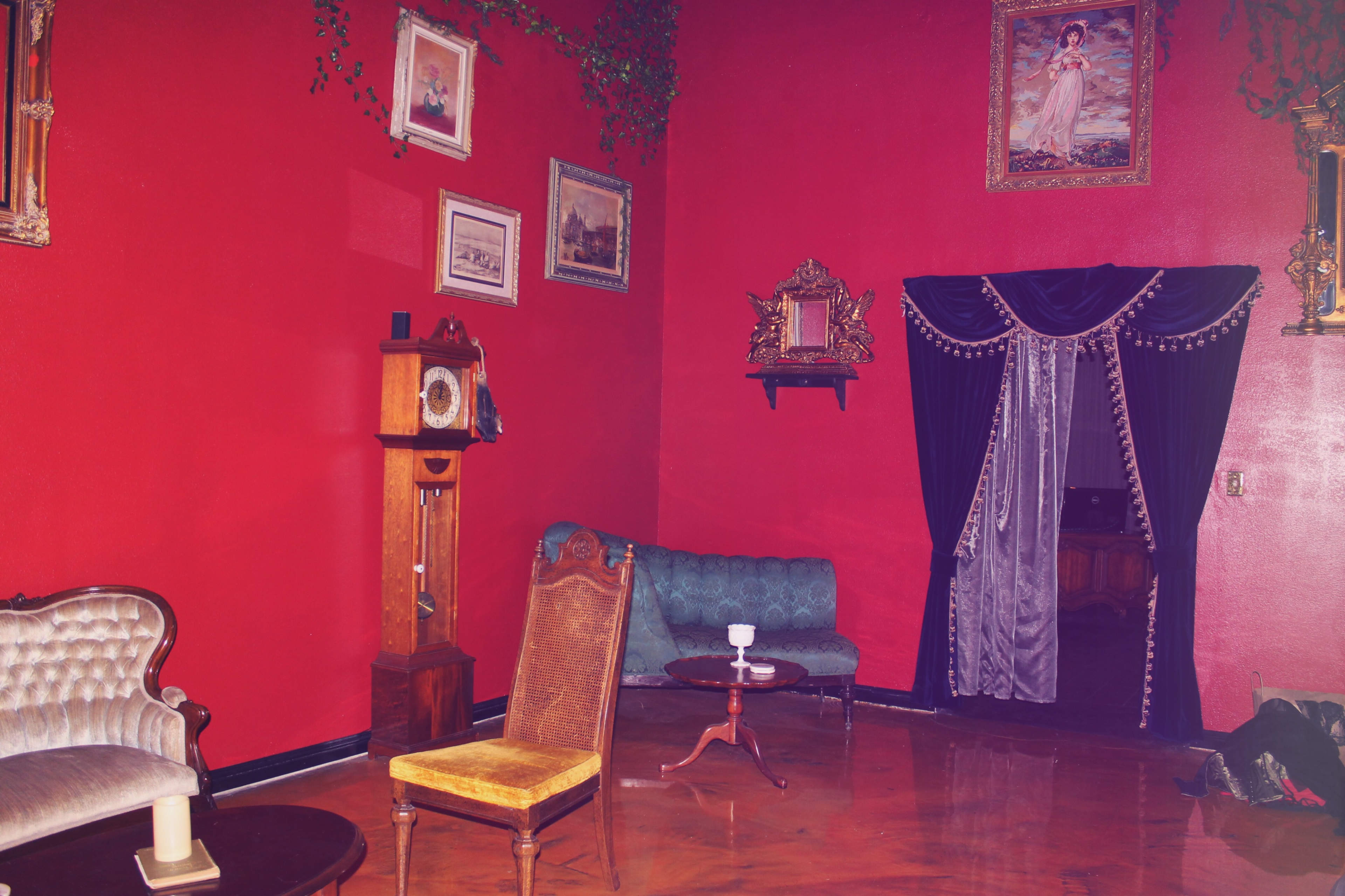 The room features red walls, vintage furniture including a green sofa and a yellow chair, and various framed artworks.