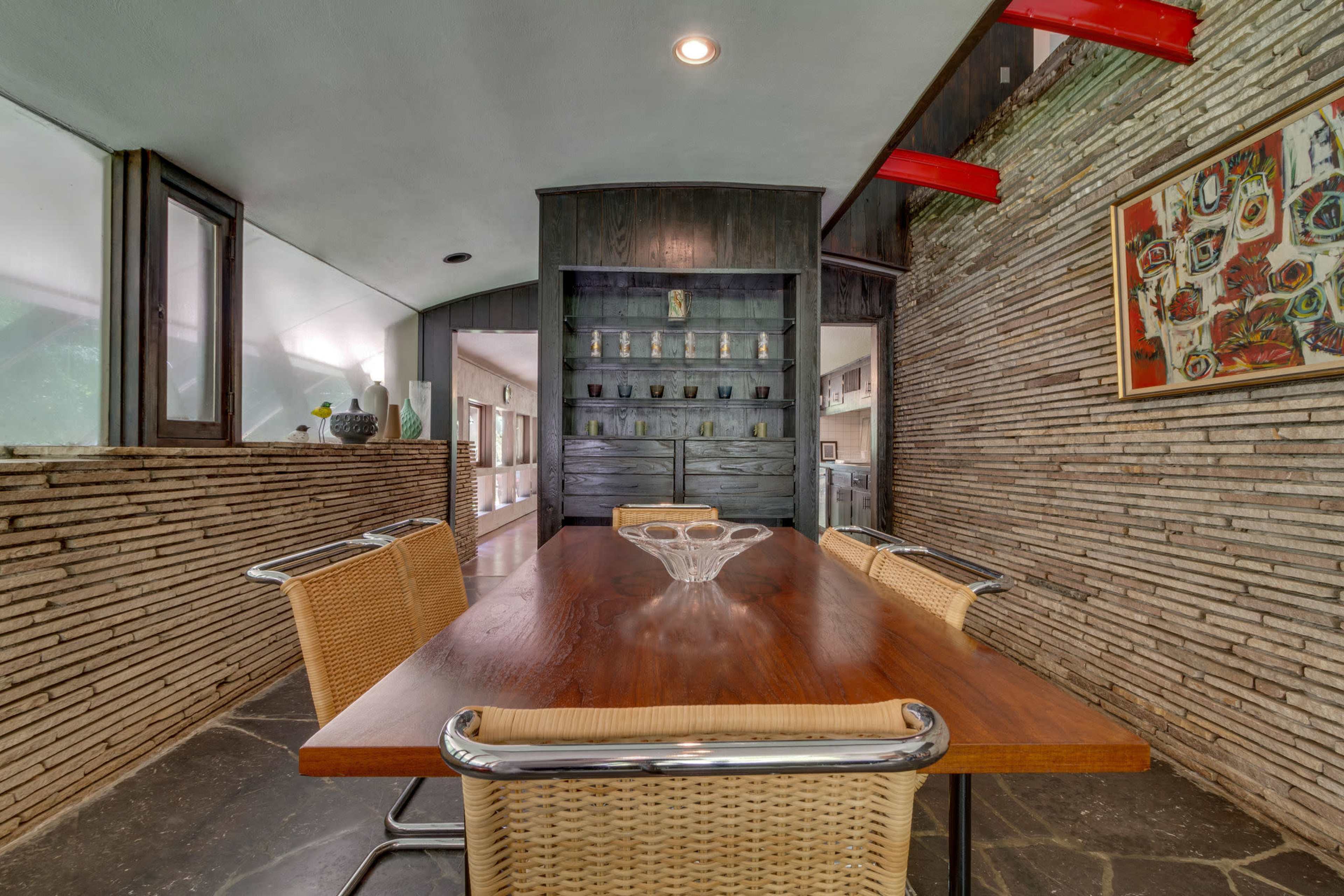 A modern dining area featuring a wooden table surrounded by four wicker chairs, set against a backdrop of textured stone walls and a built-in cabinet.