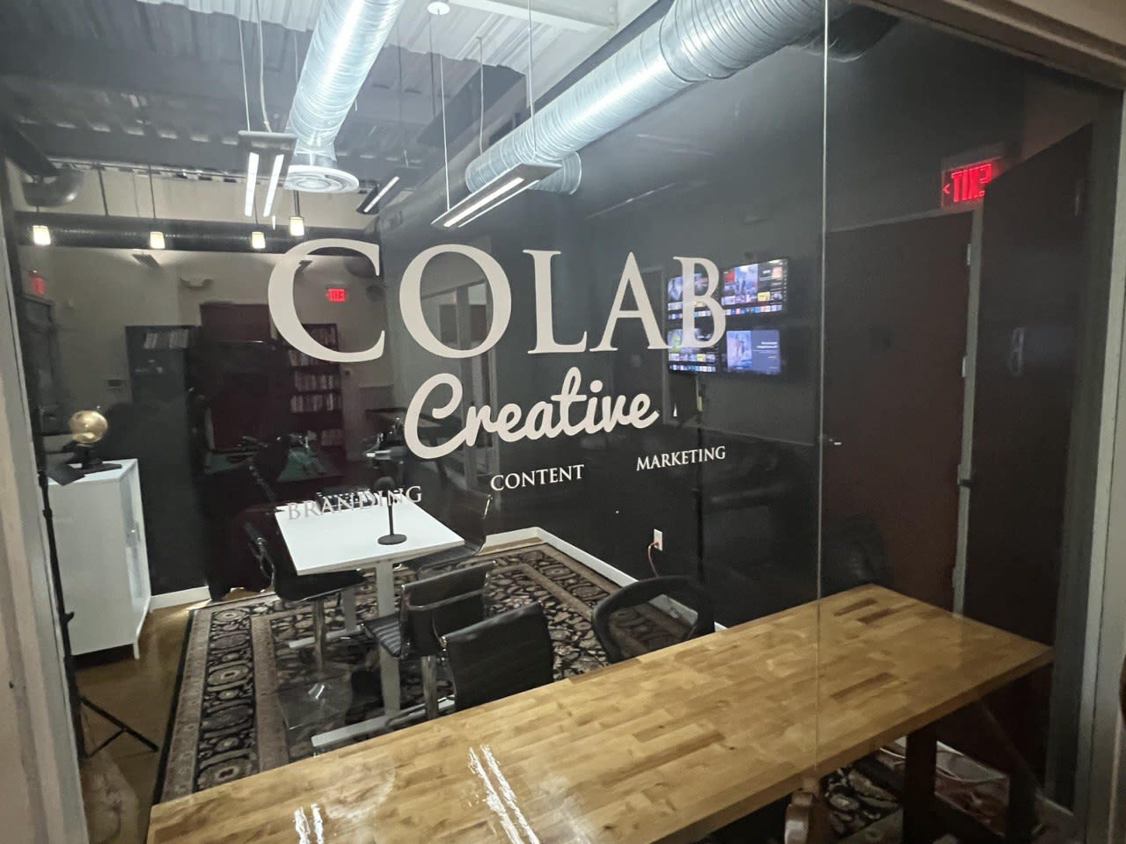 A glass-walled office with the text "COLAB Creative" prominently displayed, featuring a meeting table and chairs inside.