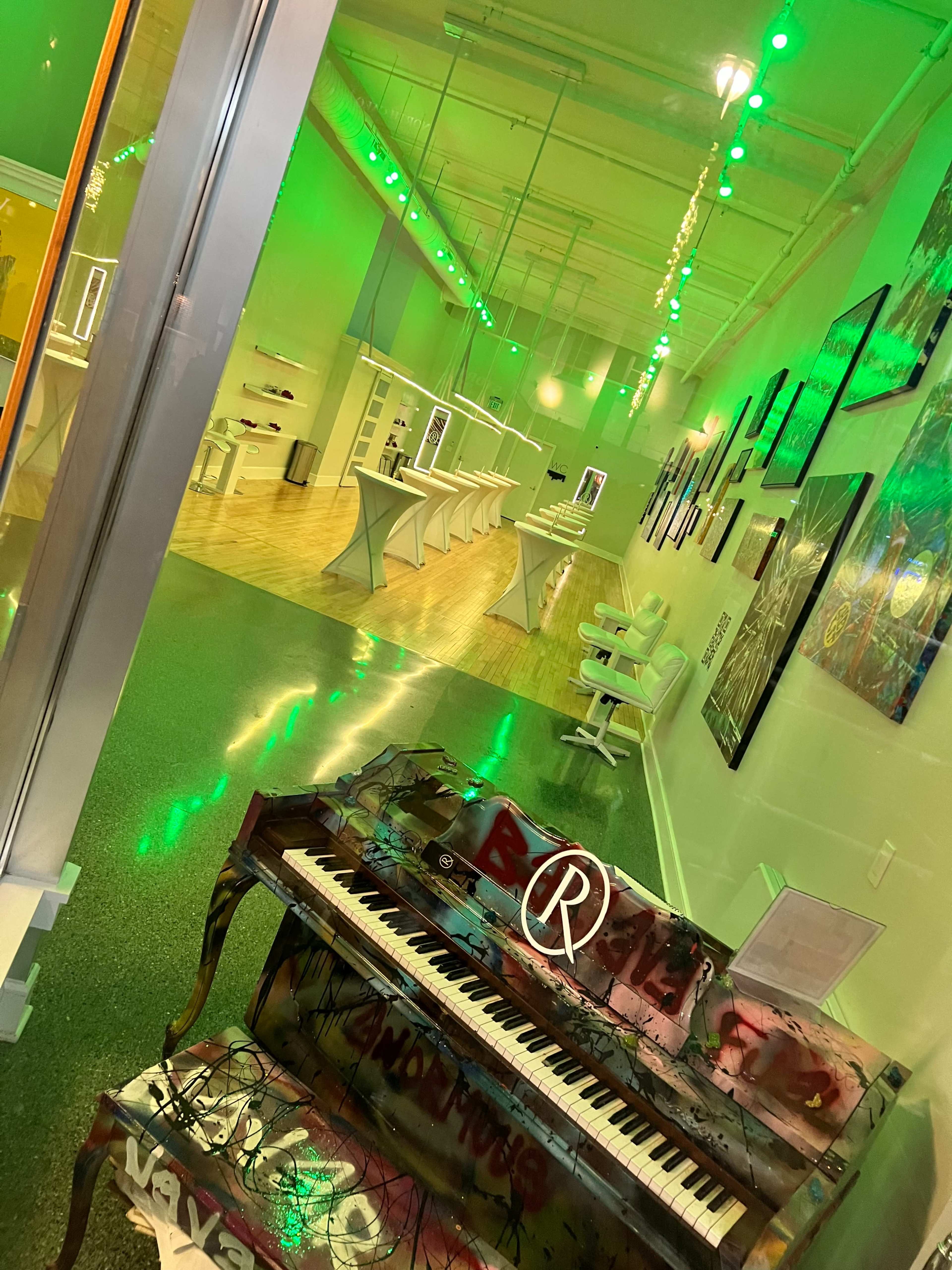 A brightly lit modern interior space featuring a colorful grand piano in the foreground and white furniture arranged along the walls.