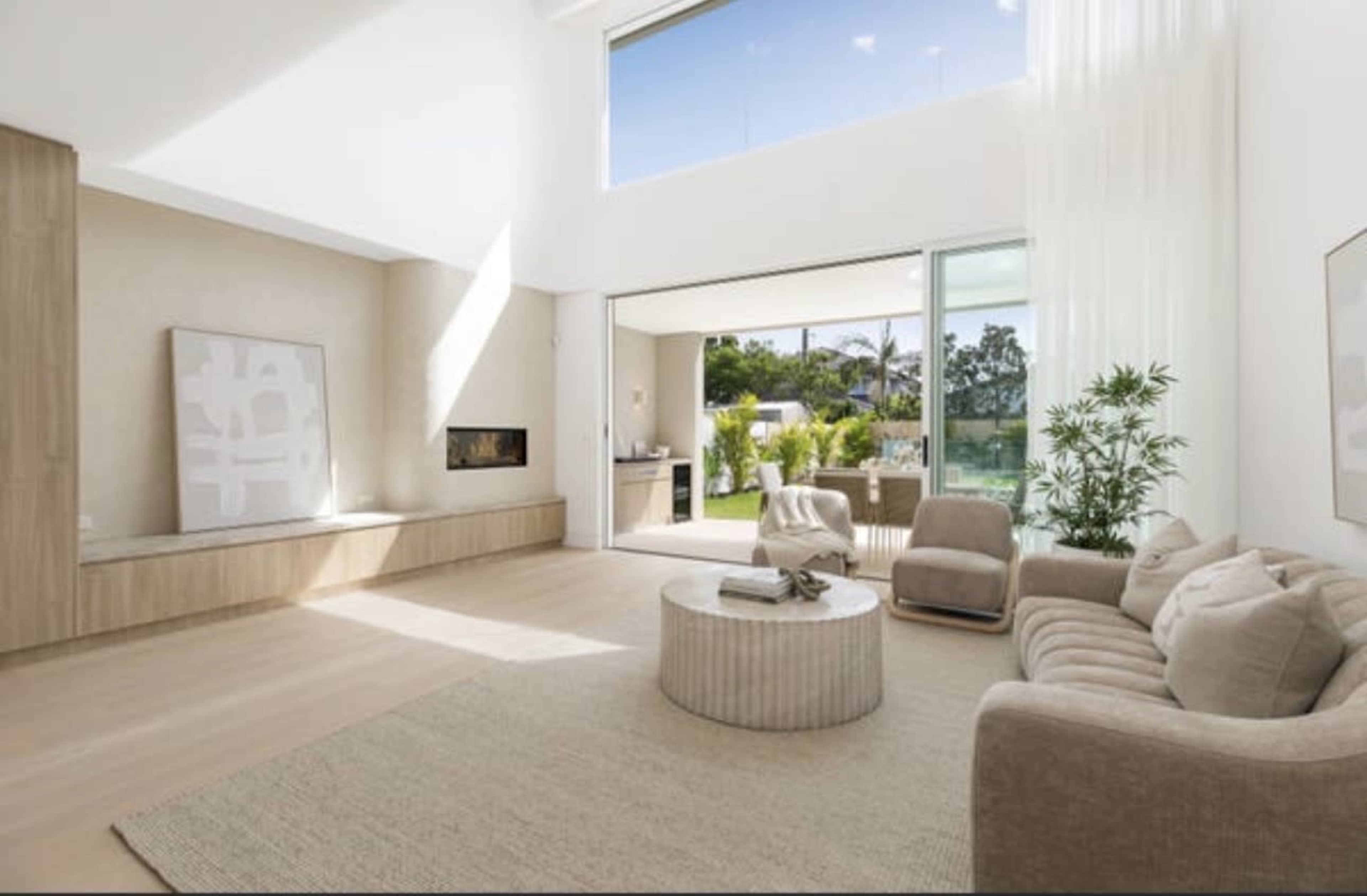 The spacious living room features large windows that open to an outdoor area, complemented by modern furniture and light-colored decor.