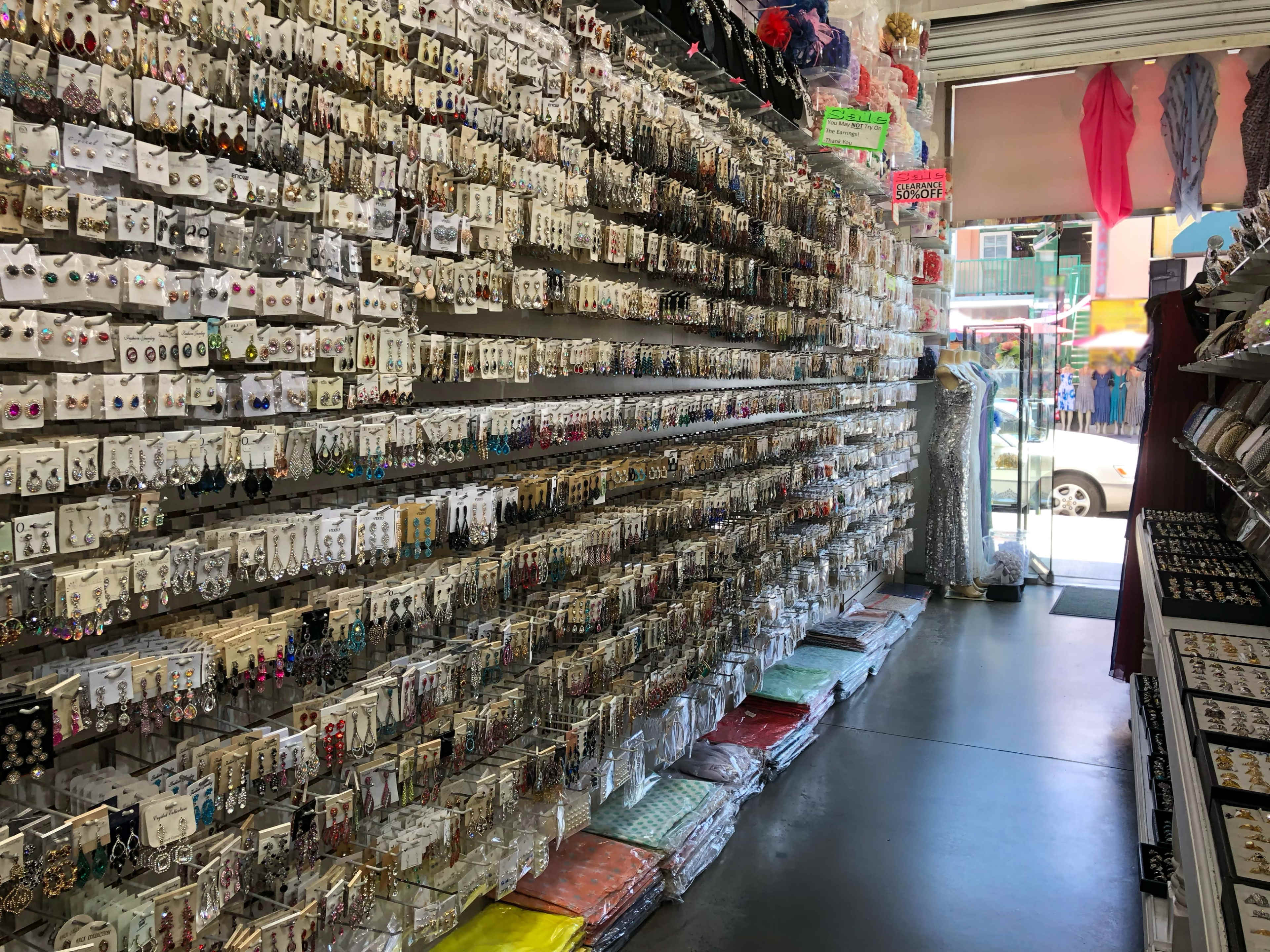 The image shows a retail store interior with a wall displaying numerous pairs of earrings on hanging cards and various fabrics stacked on the floor.