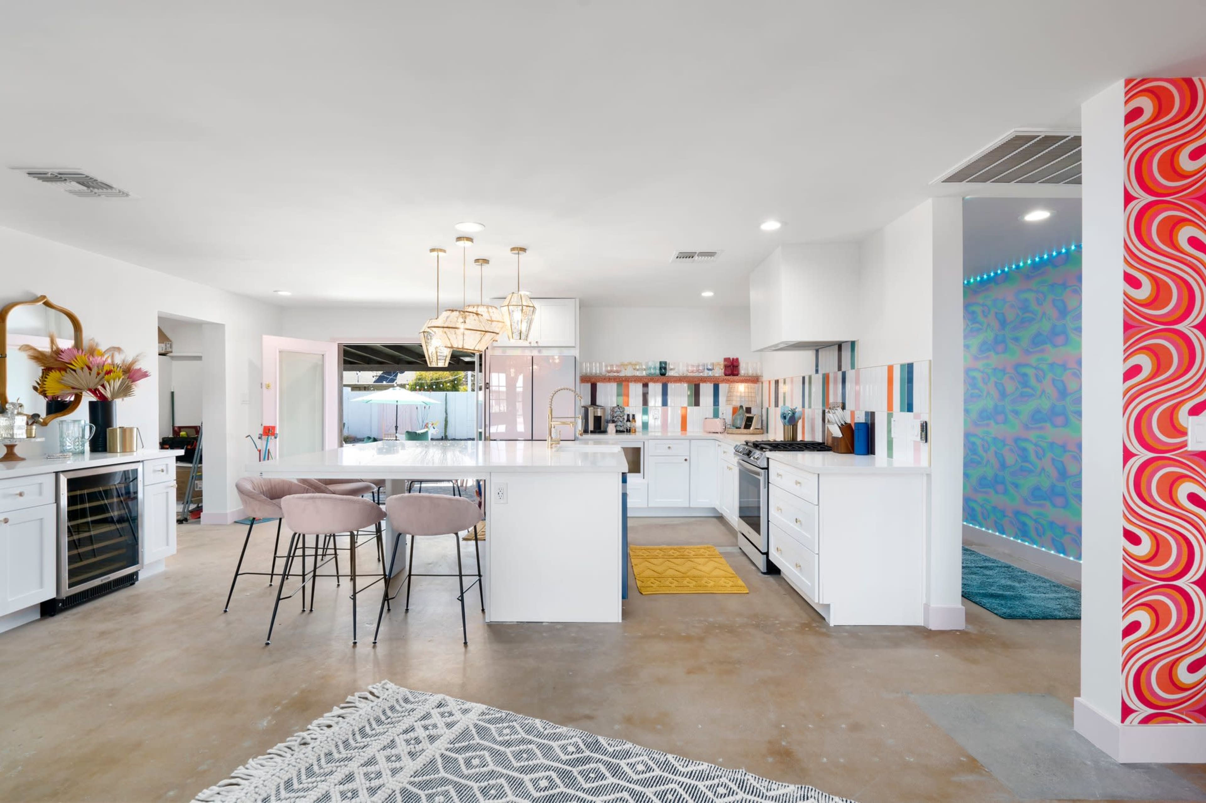 A modern kitchen features white cabinetry, colorful tile accents, and a dining area with pink bar stools.
