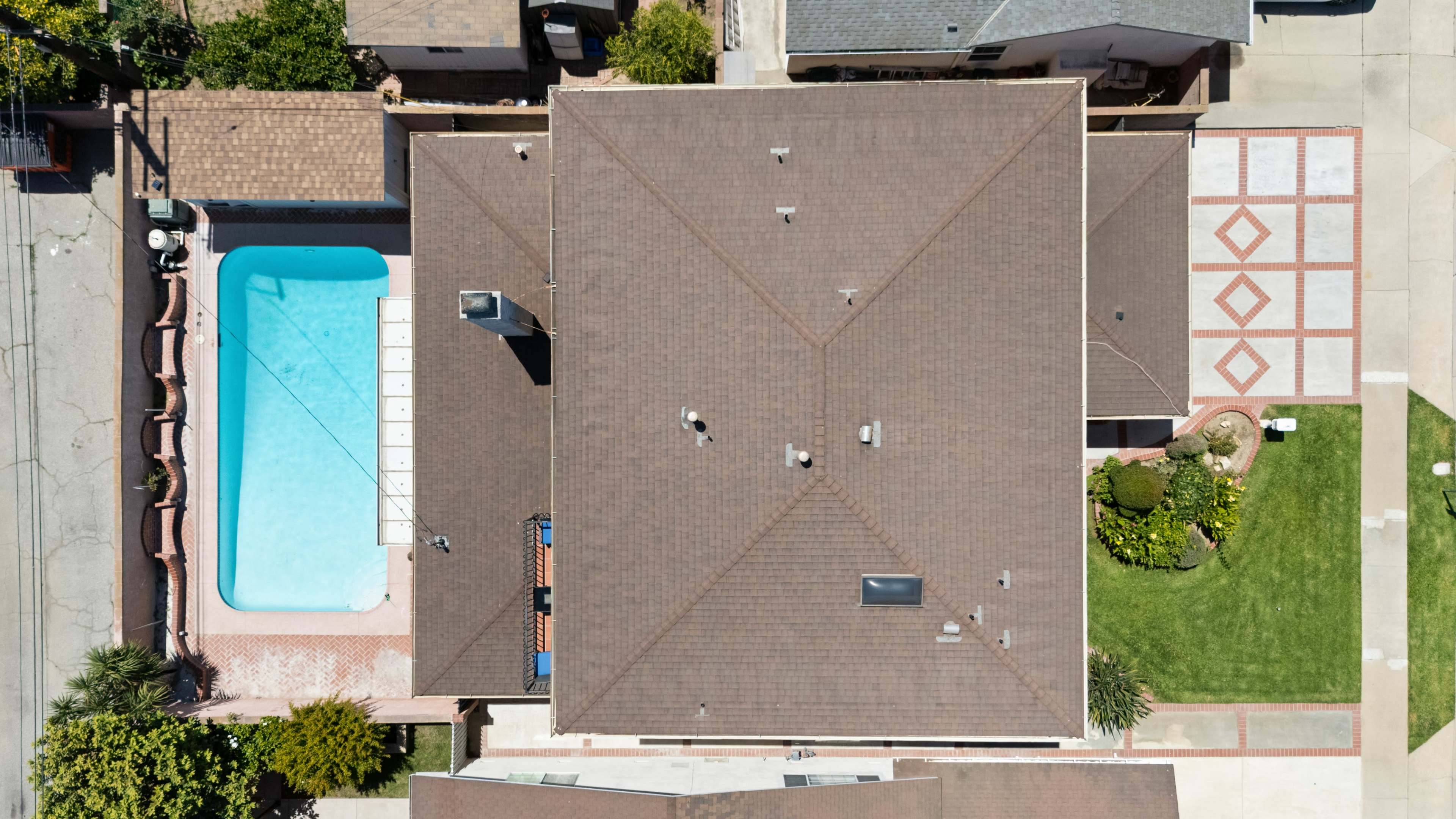 The image shows an aerial view of a residential property featuring a swimming pool, surrounded by landscaped areas and concrete patios.