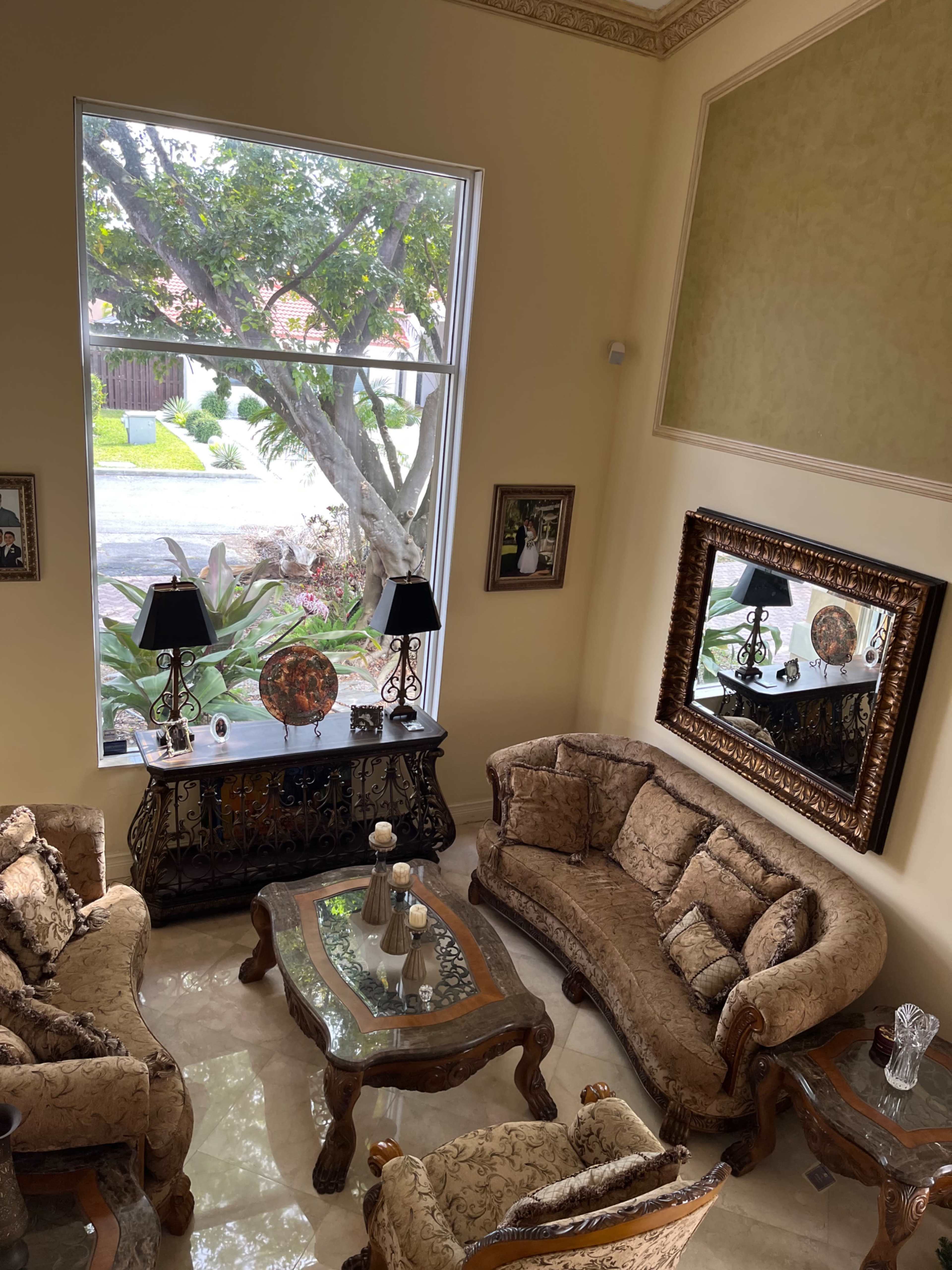 A well-furnished living room with ornate furniture, a large mirror, and a view of the outdoor greenery through a large window.