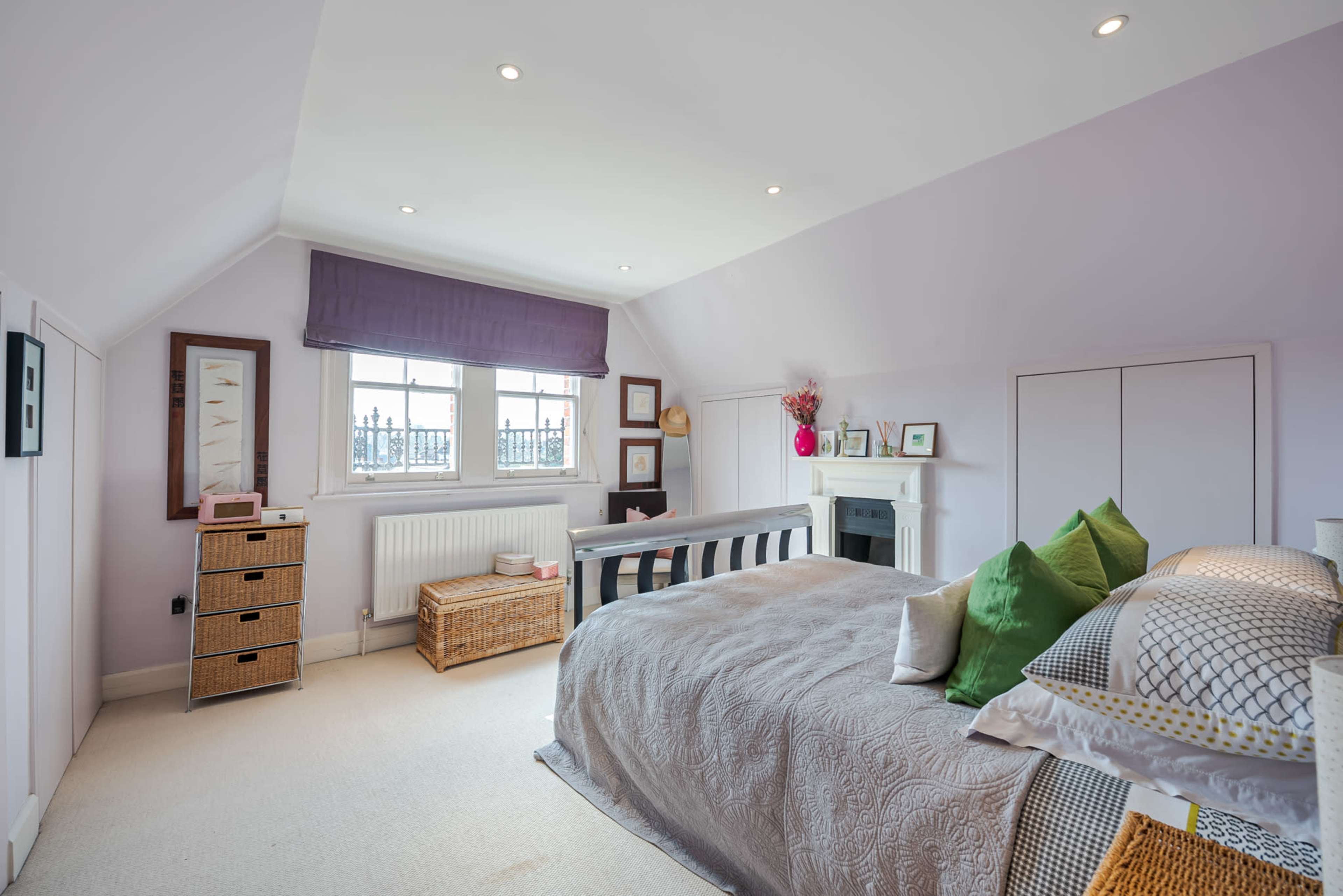 A spacious bedroom features a large bed, a fireplace, and organized storage solutions, with light-colored walls and large windows.