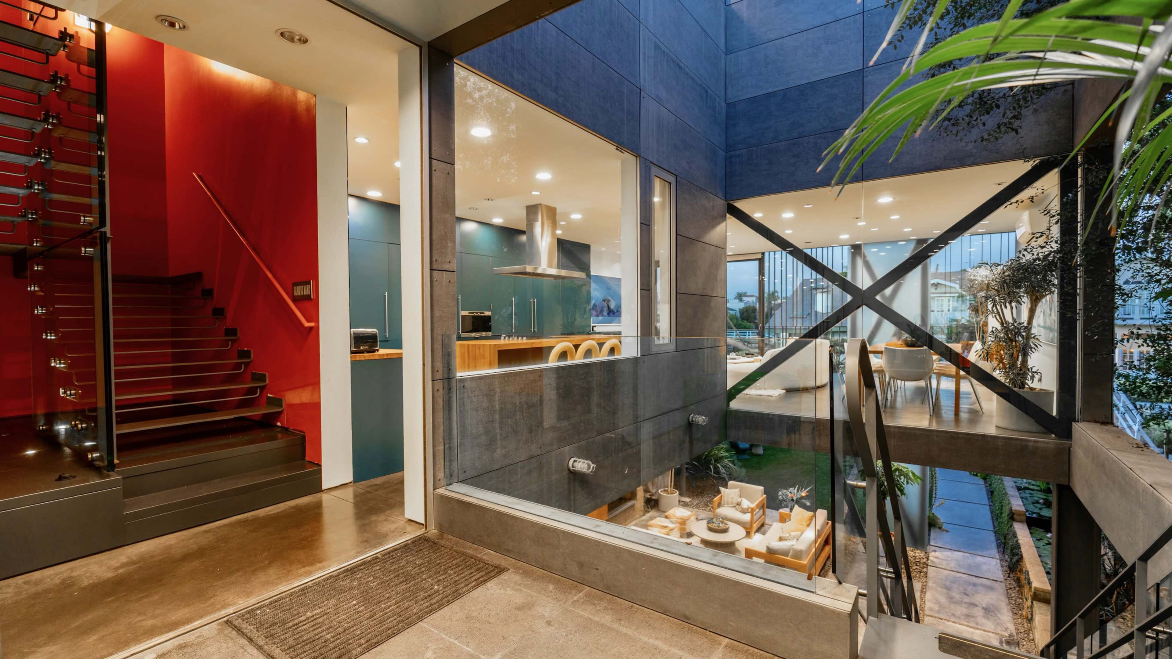 A modern, multi-level home with a spacious entrance featuring a staircase and large glass walls that overlook a garden area.