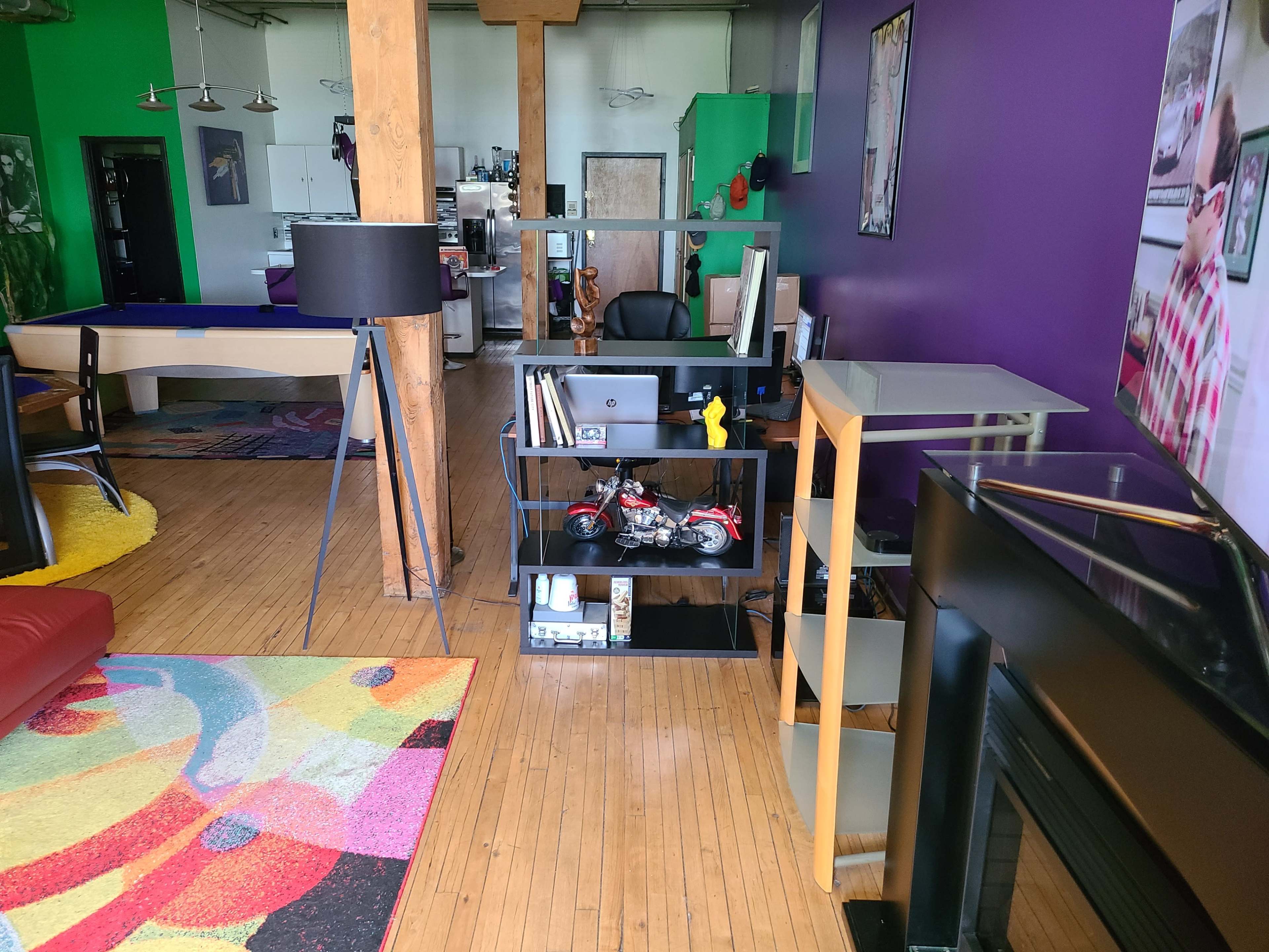 A modern room with wooden floors featuring various furniture, including a desk, shelves with decorative items, and a colorful area rug.