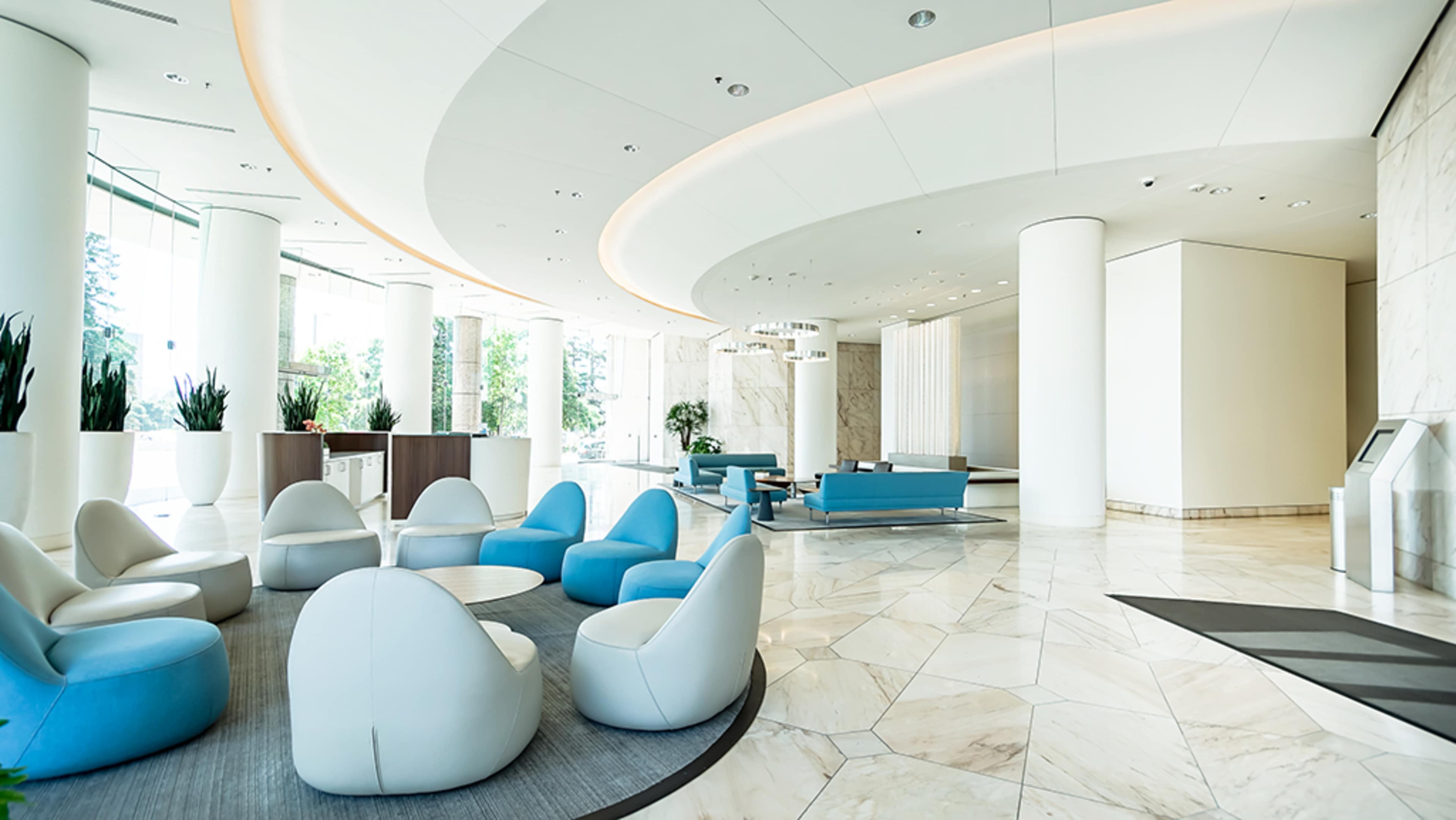 A modern lounge area featuring white marble floors, curved ceilings, and blue and white seating arrangements.