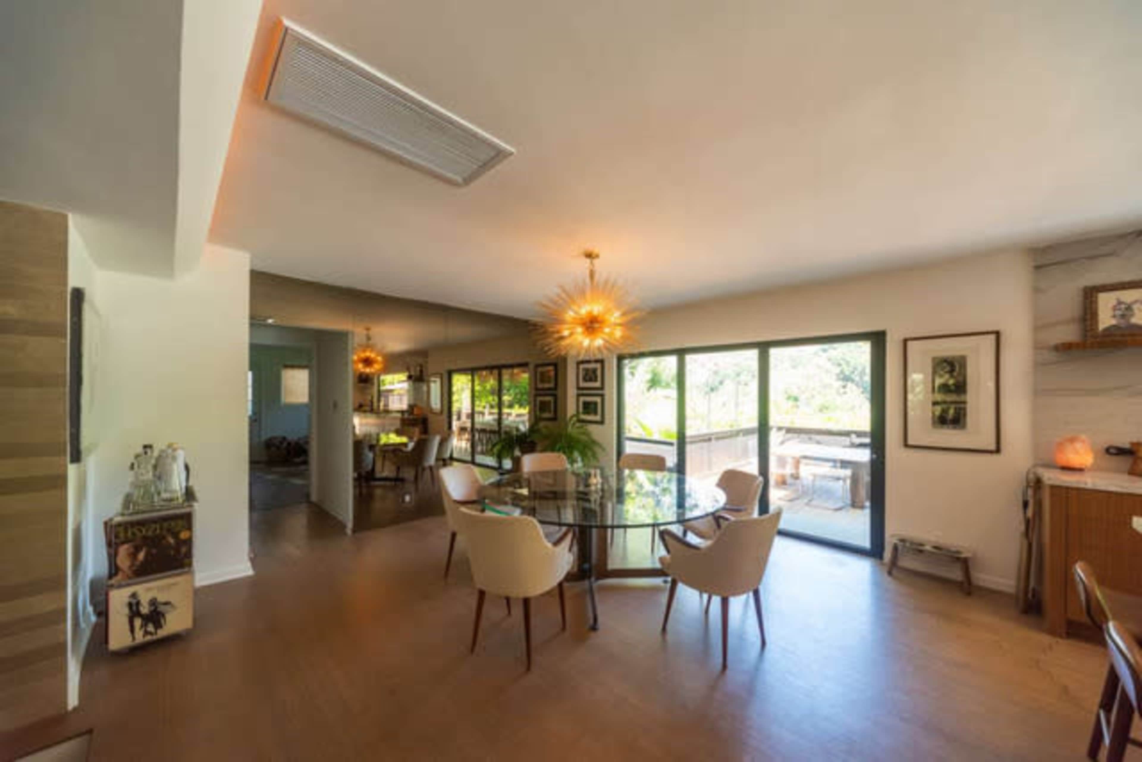 A modern dining area features a round glass table surrounded by upholstered chairs, with sliding glass doors providing access to a patio and ample natural light.
