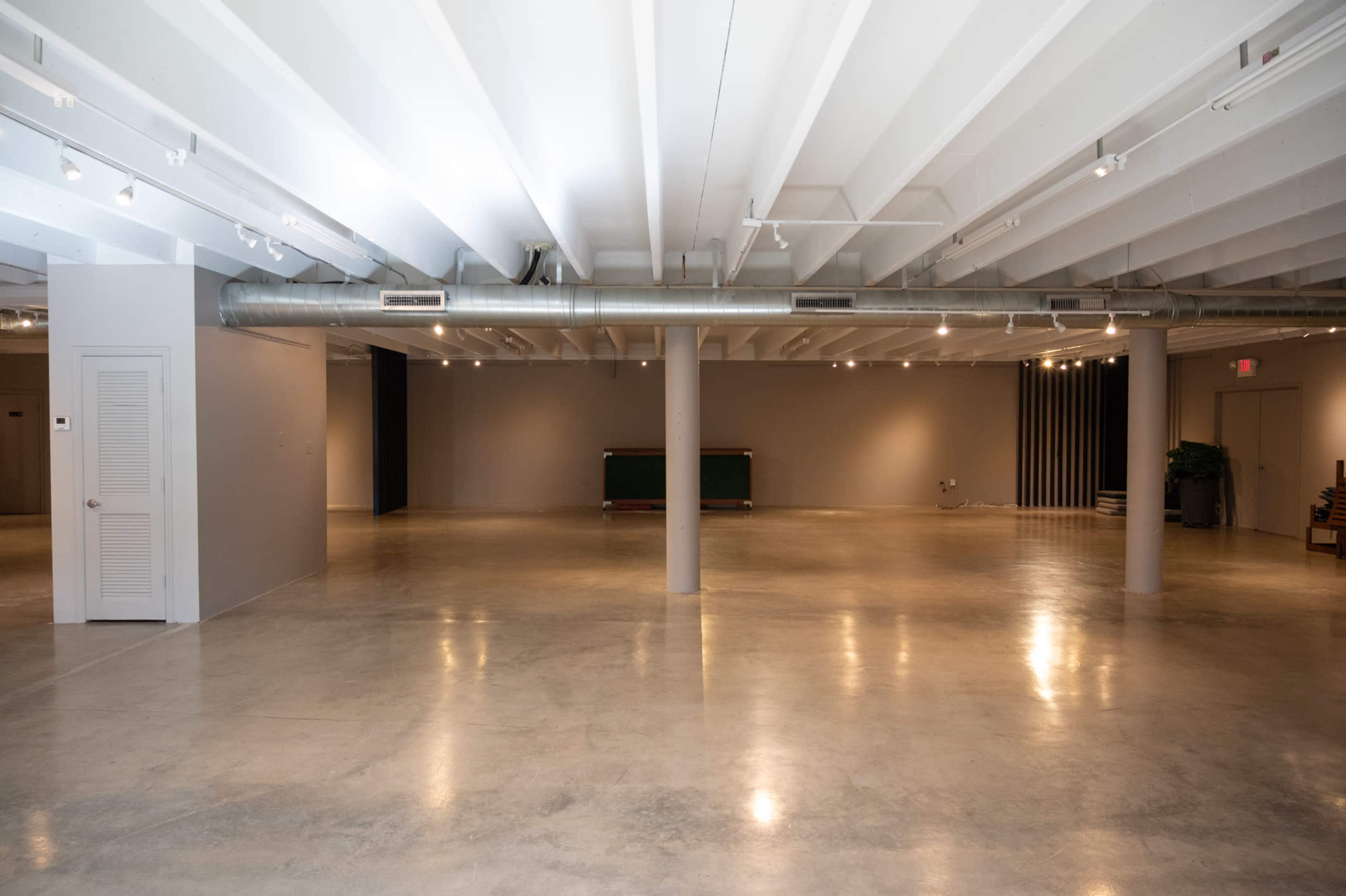 The image shows an empty, spacious interior with exposed beams, polished concrete flooring, and several columns throughout the area.
