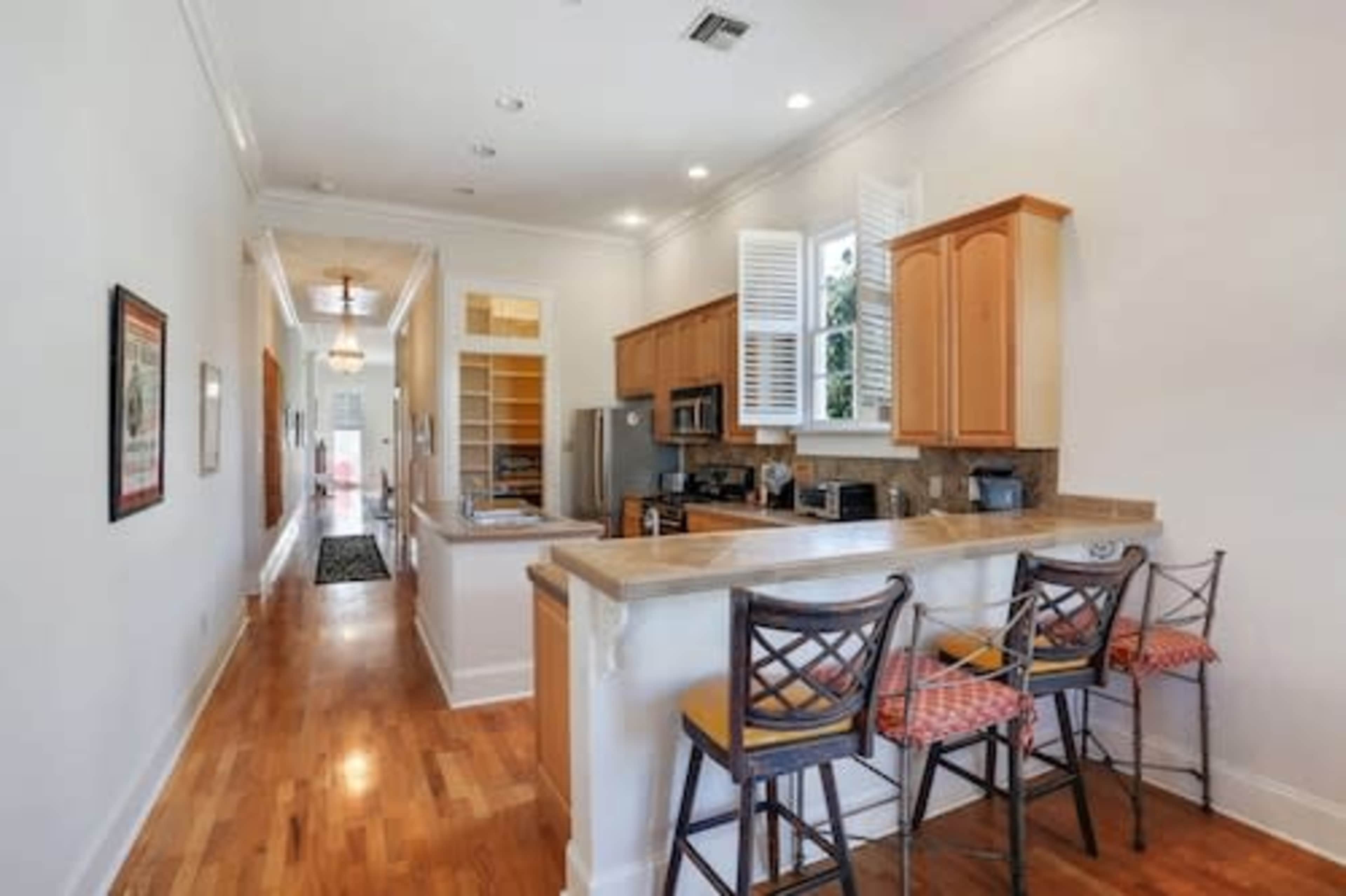A modern kitchen with wooden cabinetry and a breakfast bar, leading to a hallway in a well-lit home.