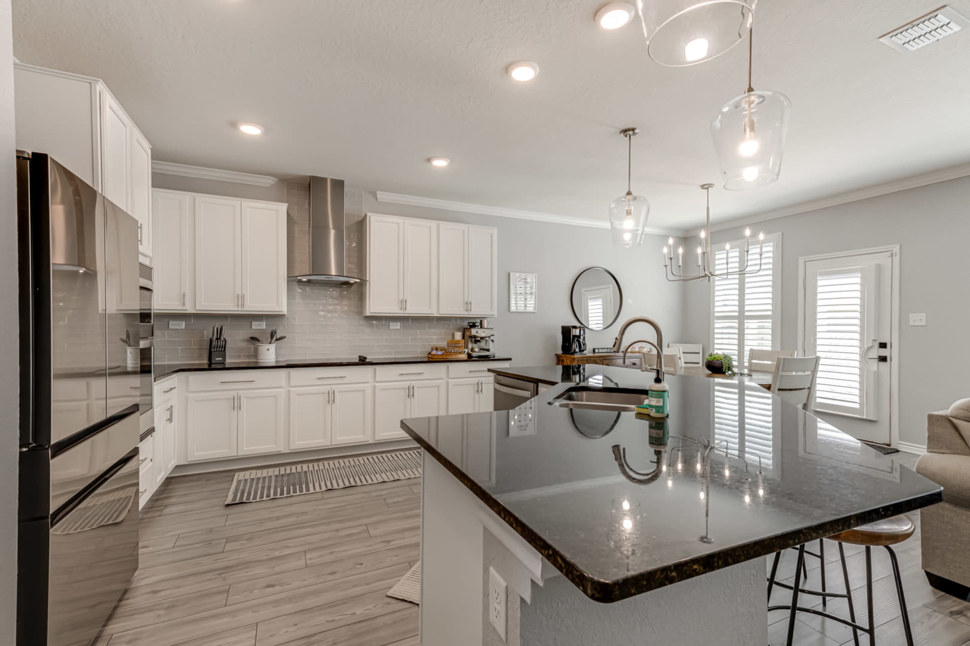 A modern kitchen features white cabinetry, a marble backsplash, and a large island with bar stools.