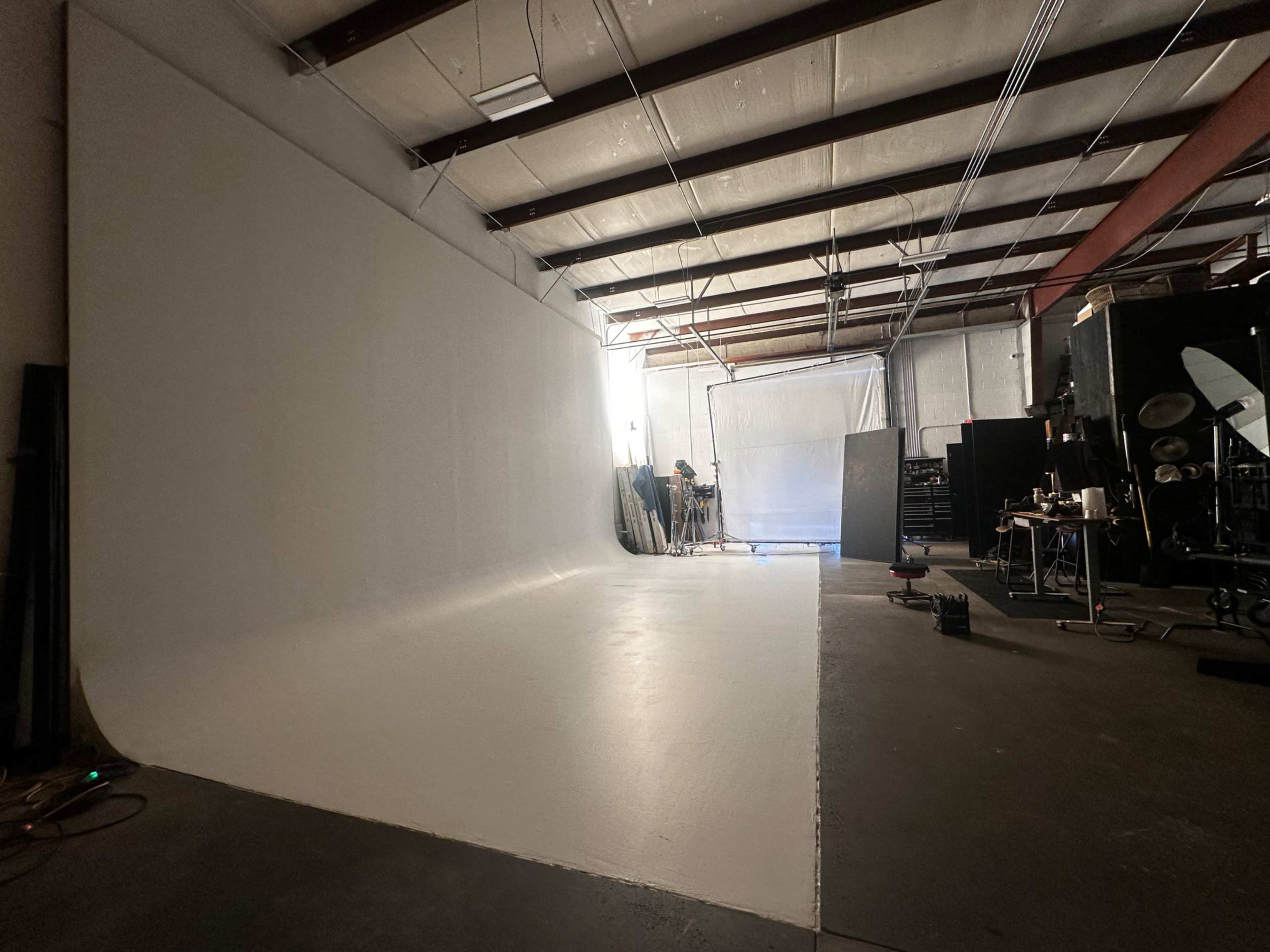 The image shows a spacious studio with a white seamless backdrop, lighting equipment, and various filmmaking gear scattered throughout.
