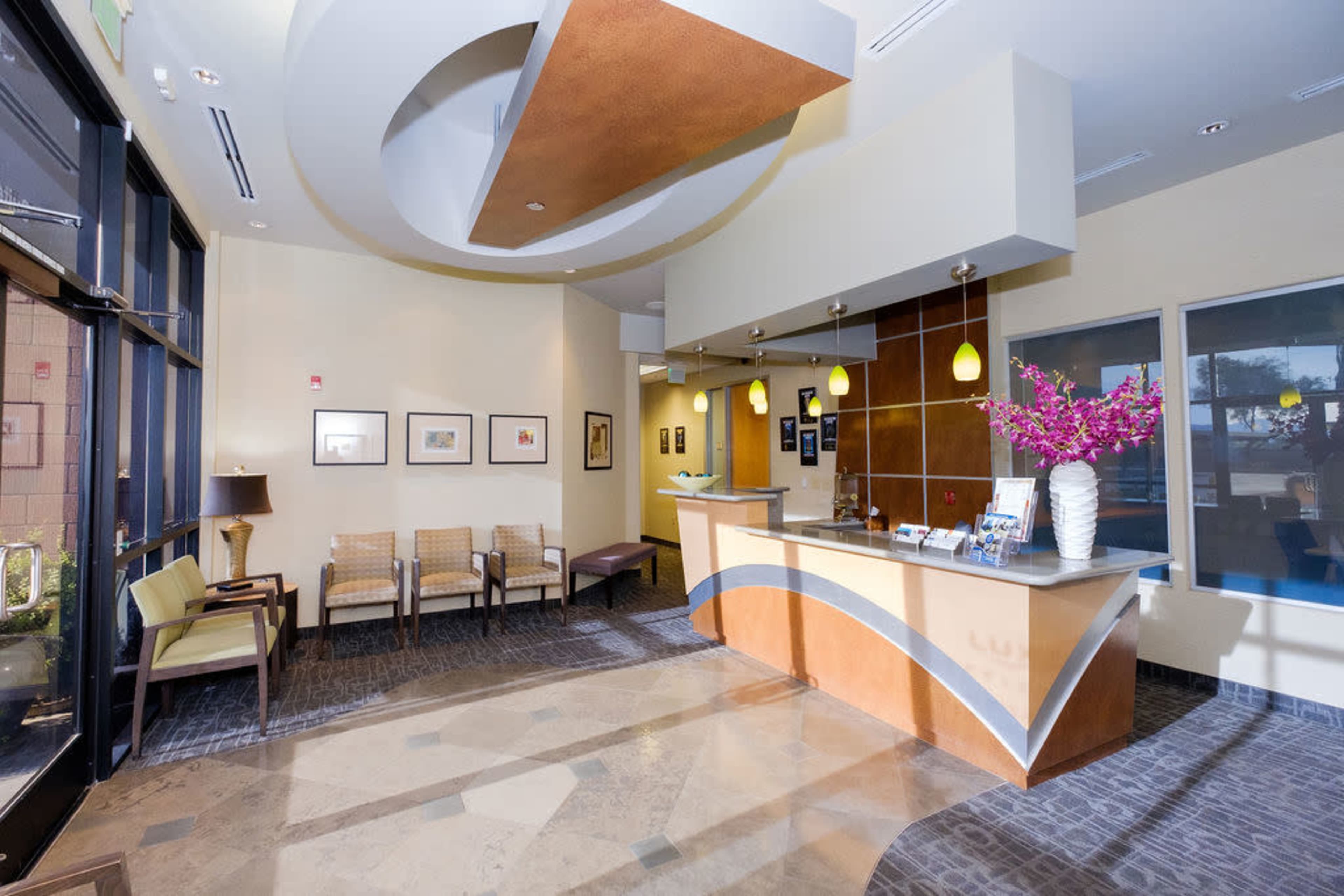 A modern reception area with a curvy front desk, comfortable seating, and decorative plants under bright lighting.