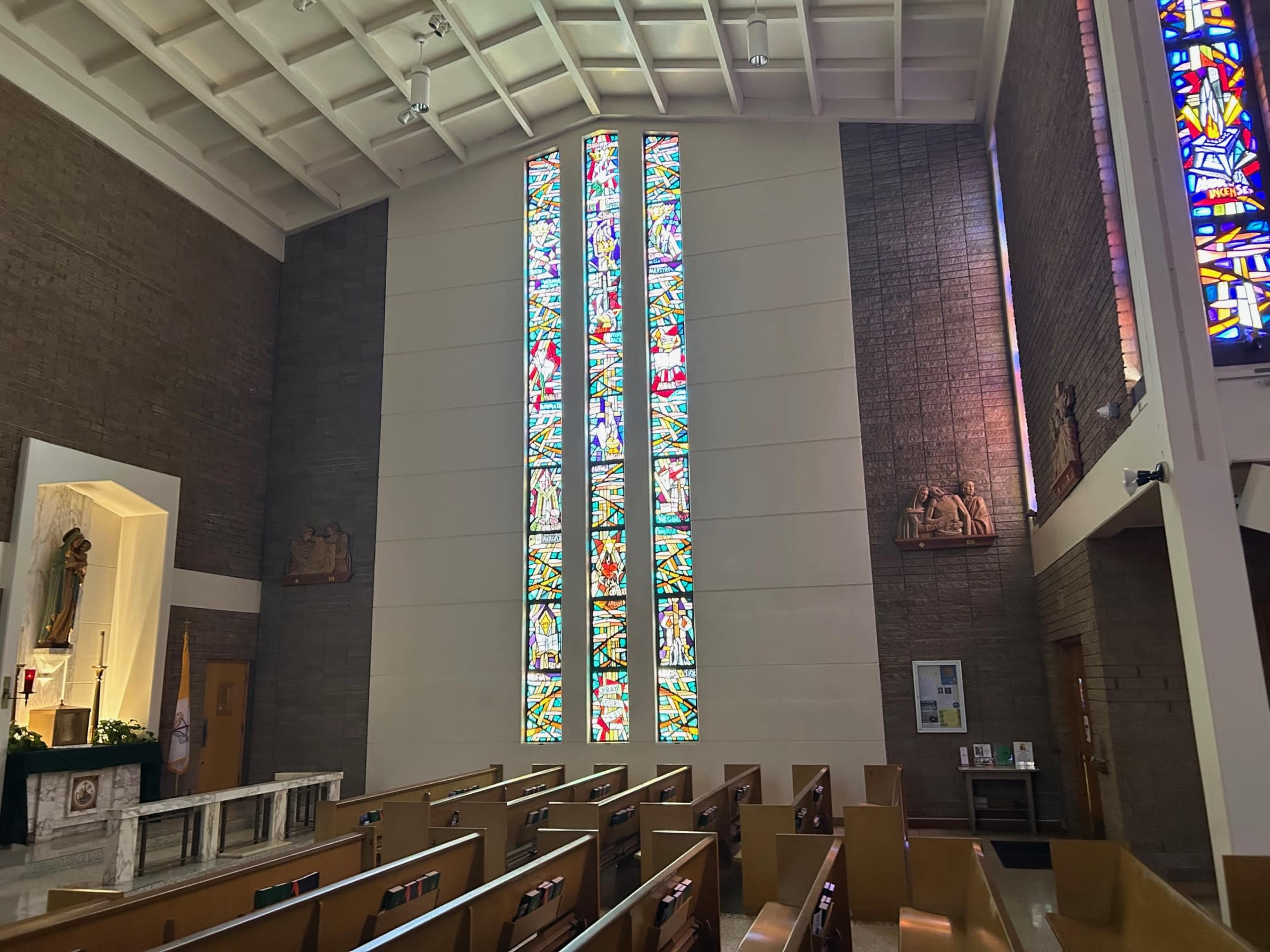 The interior of a modern church features colorful stained glass windows and wooden pews arranged in rows.