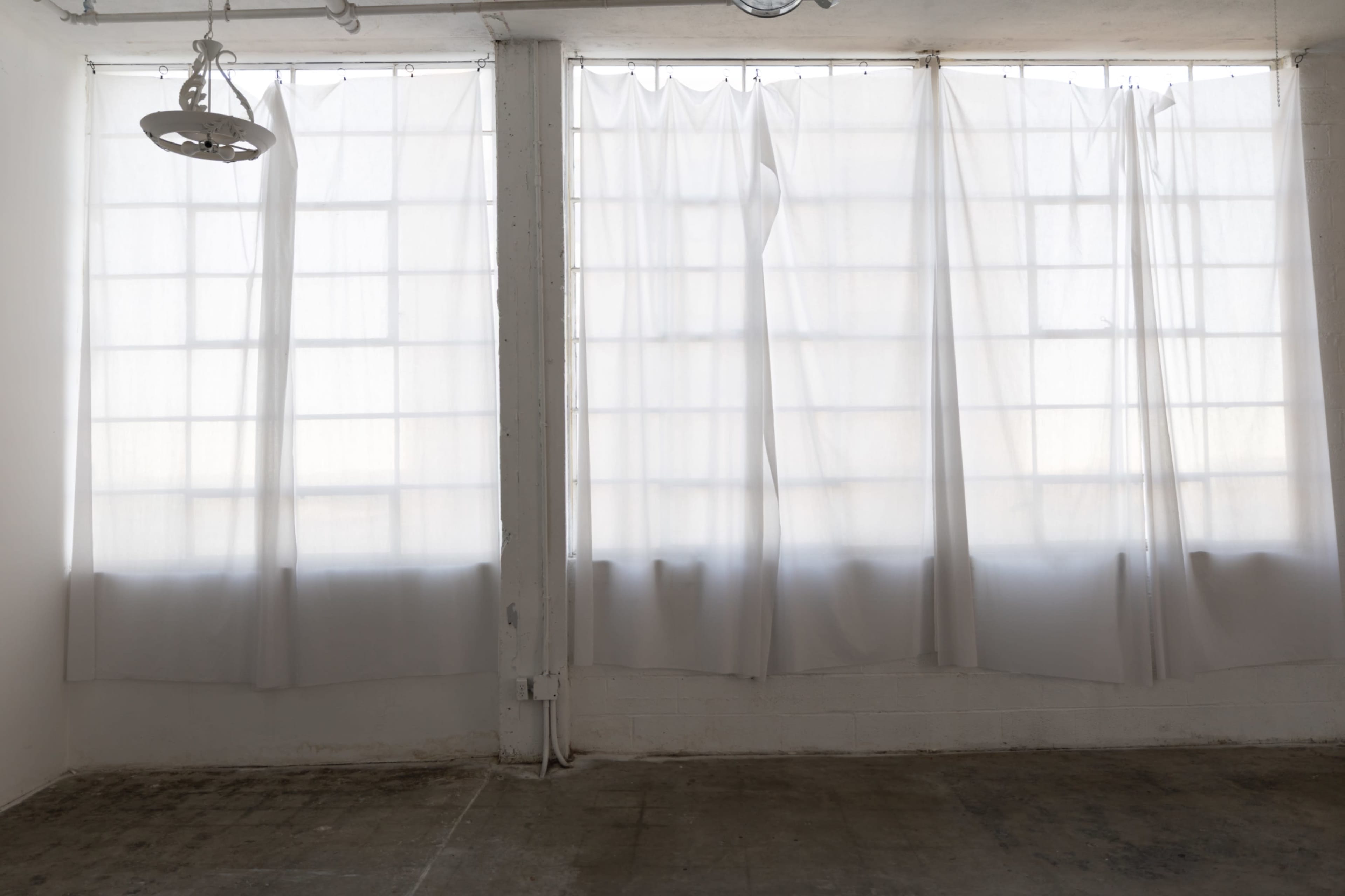 The image shows a room with large windows covered by sheer white curtains, allowing light to filter through.