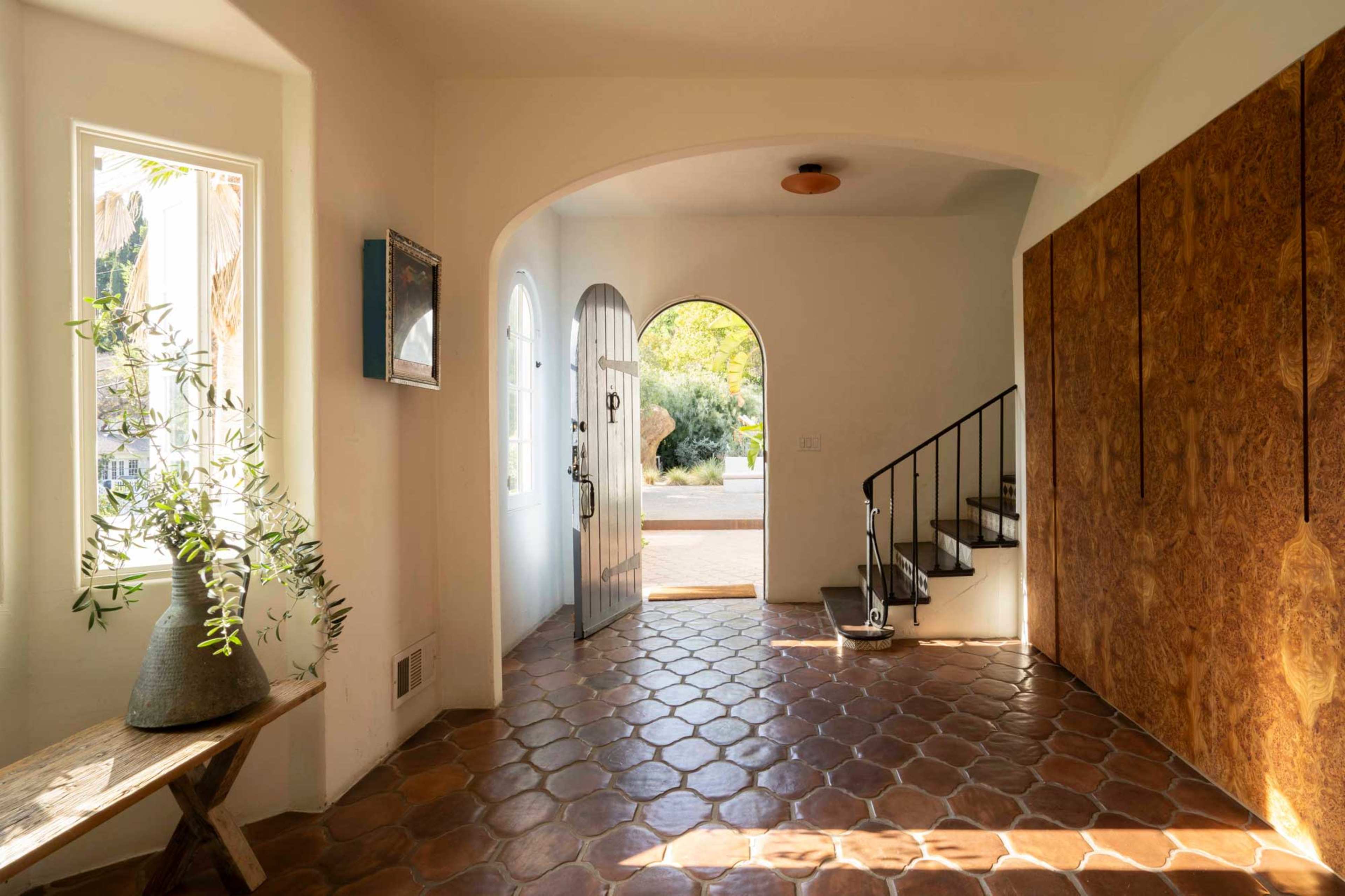 A bright entryway with tiled flooring, an open door leading outside, and a staircase on the right.