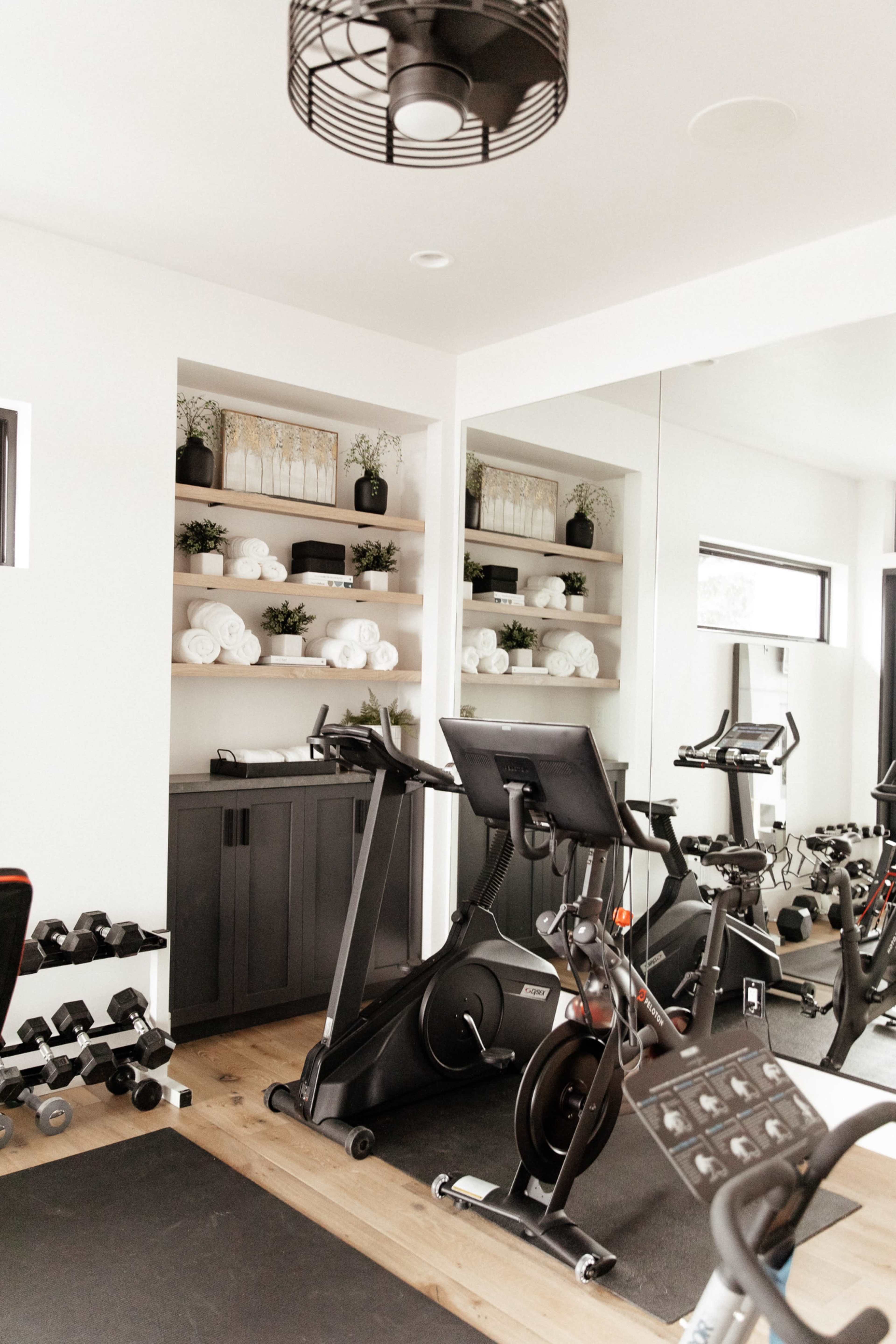 A modern home gym featuring exercise equipment, including a stationary bike and free weights, with neatly arranged shelves displaying towels and plants.
