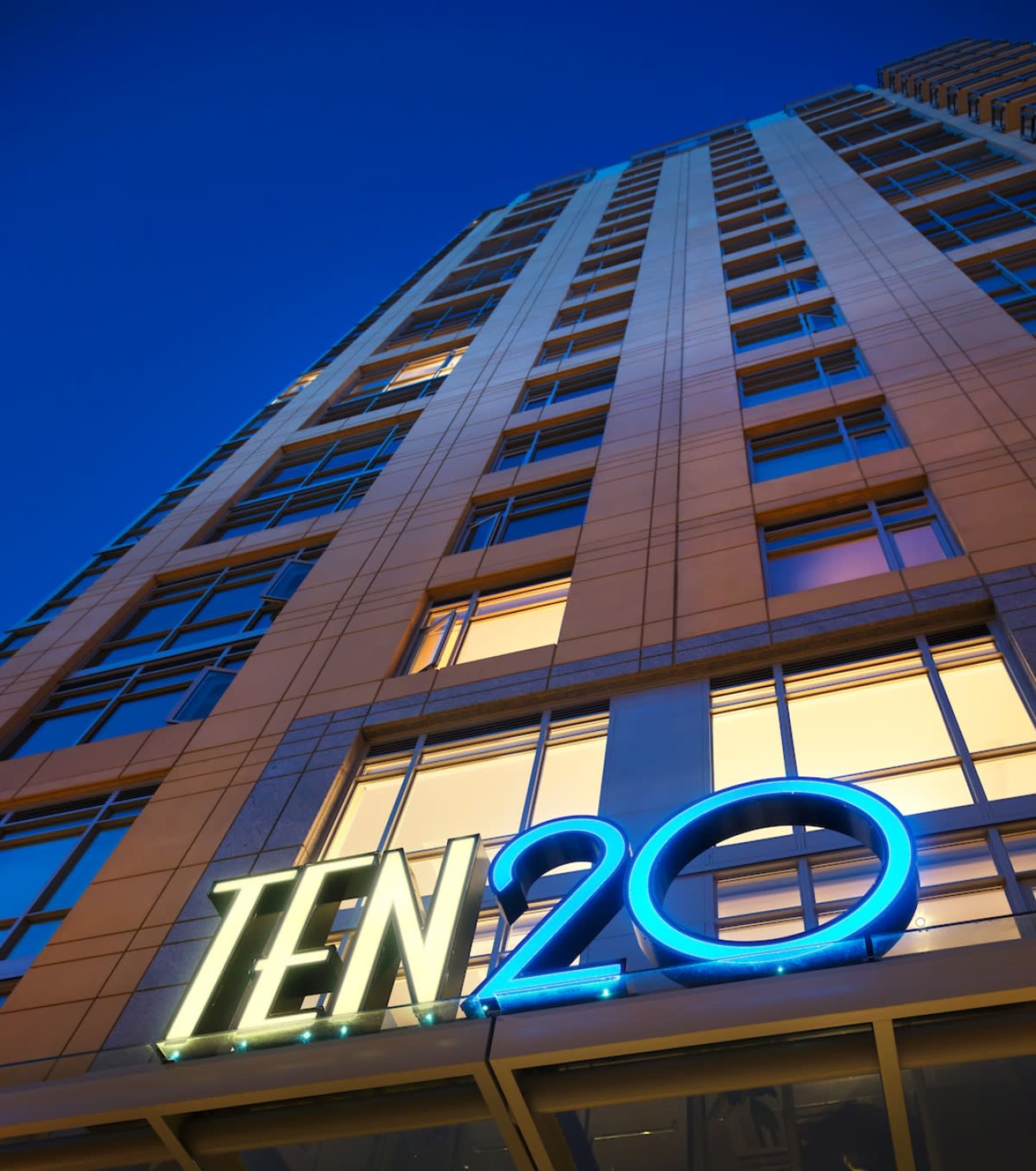 A tall building at dusk with the name "TEN20" illuminated in bright blue and green lights.