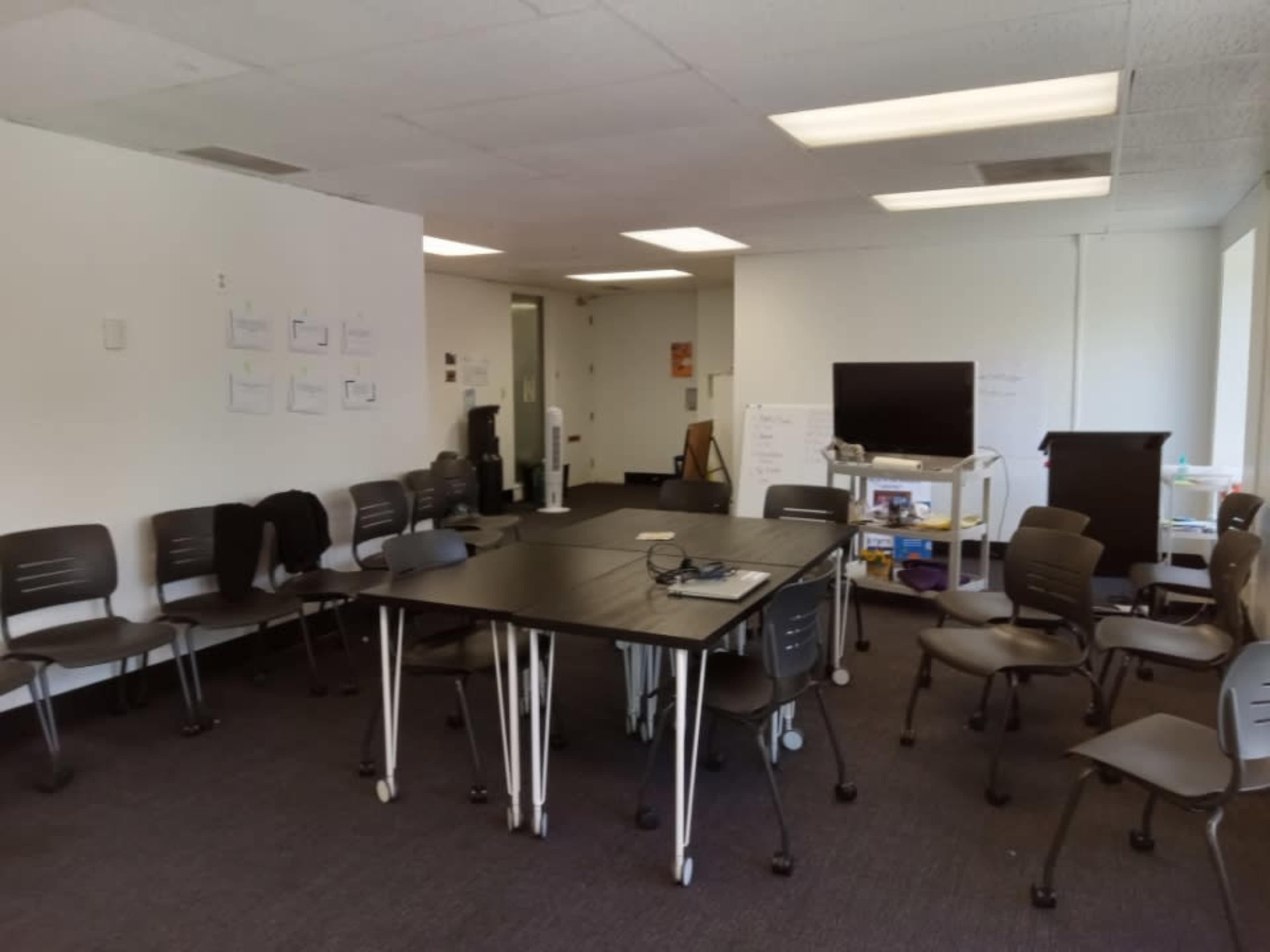 A meeting room is set up with a central table surrounded by chairs, and a television on one side of the room.