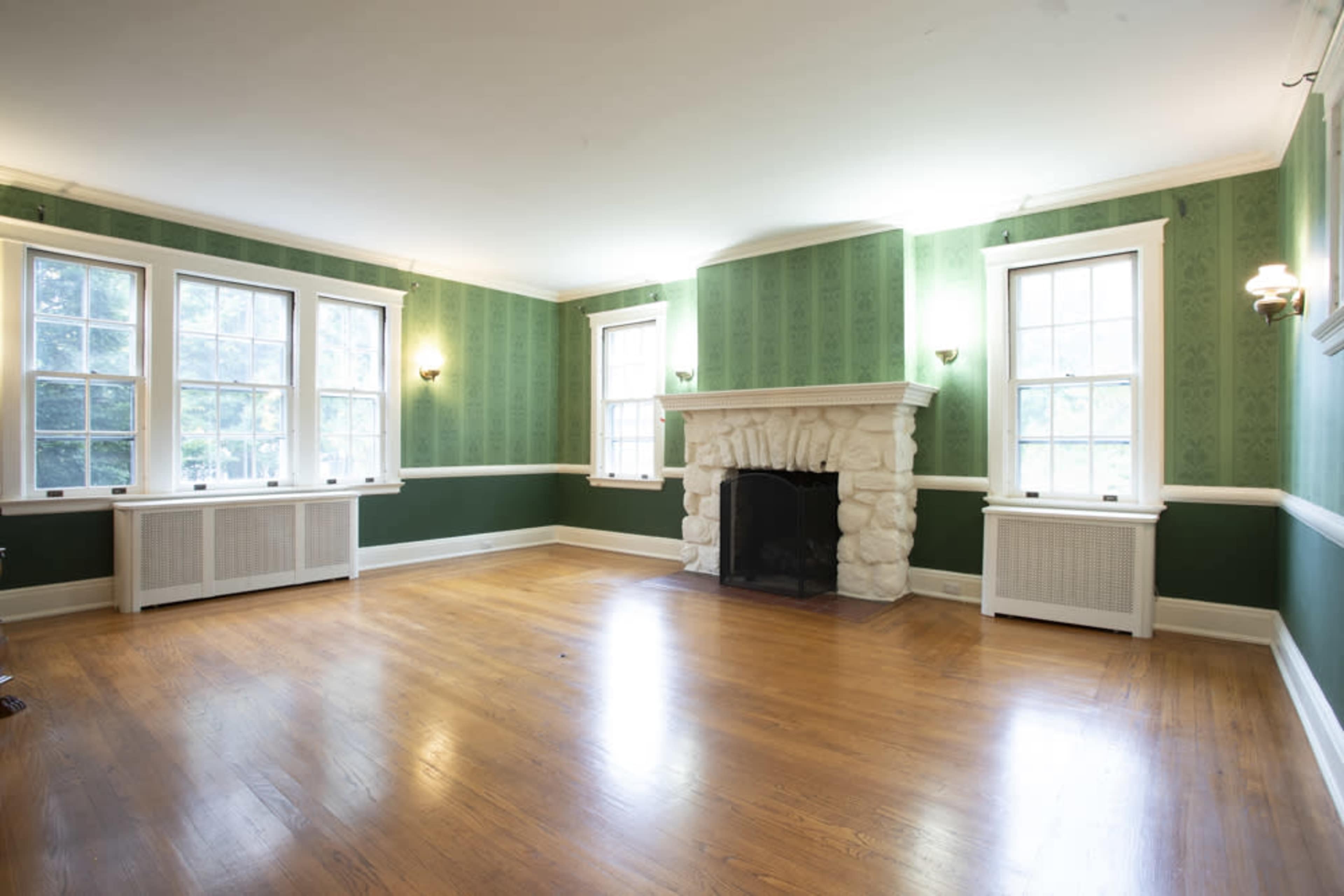 The room features green wallpaper, large windows, a stone fireplace, and hardwood flooring.