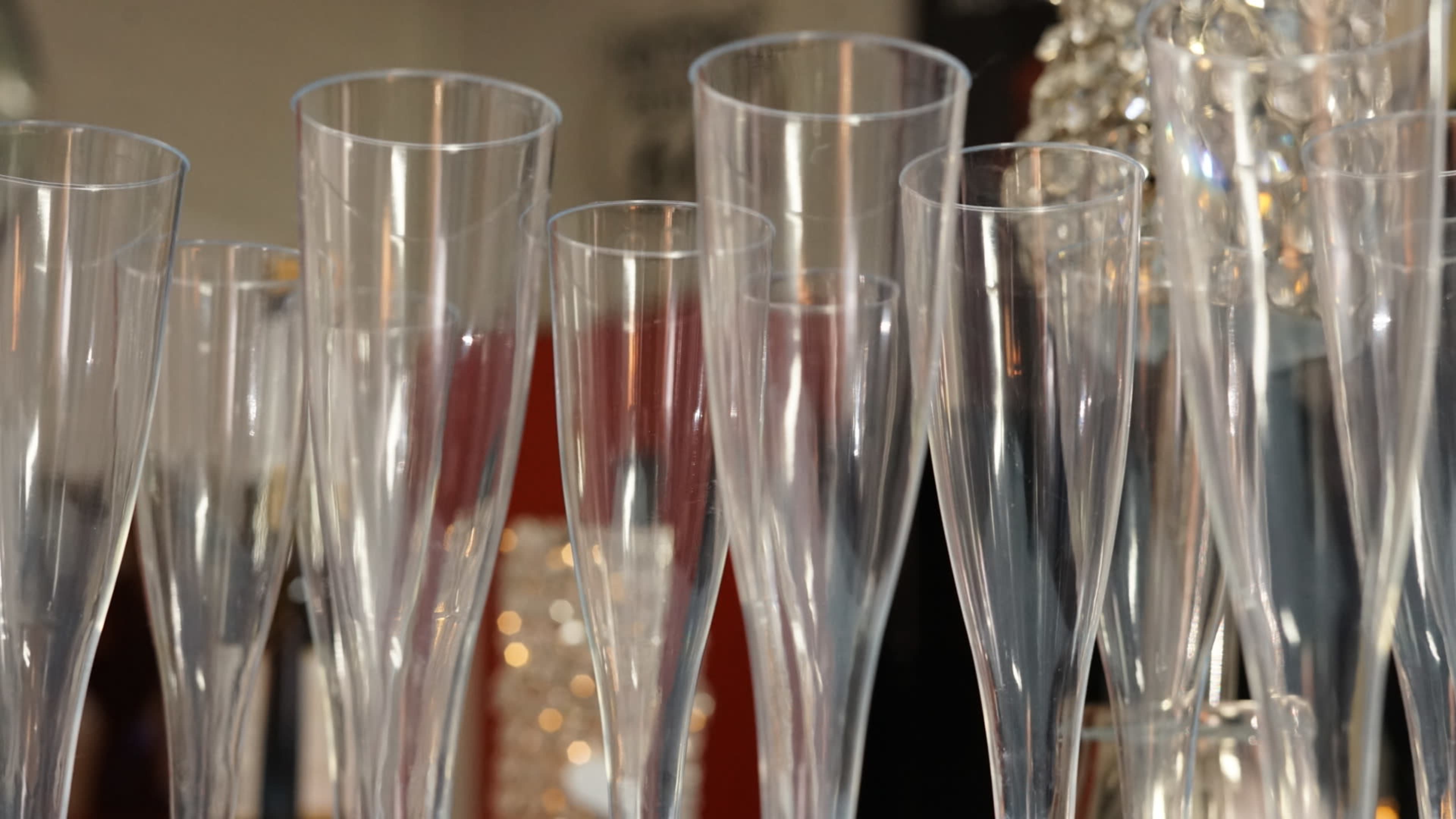 A row of clear champagne flutes is arranged on a table, reflecting soft light from nearby decorations.