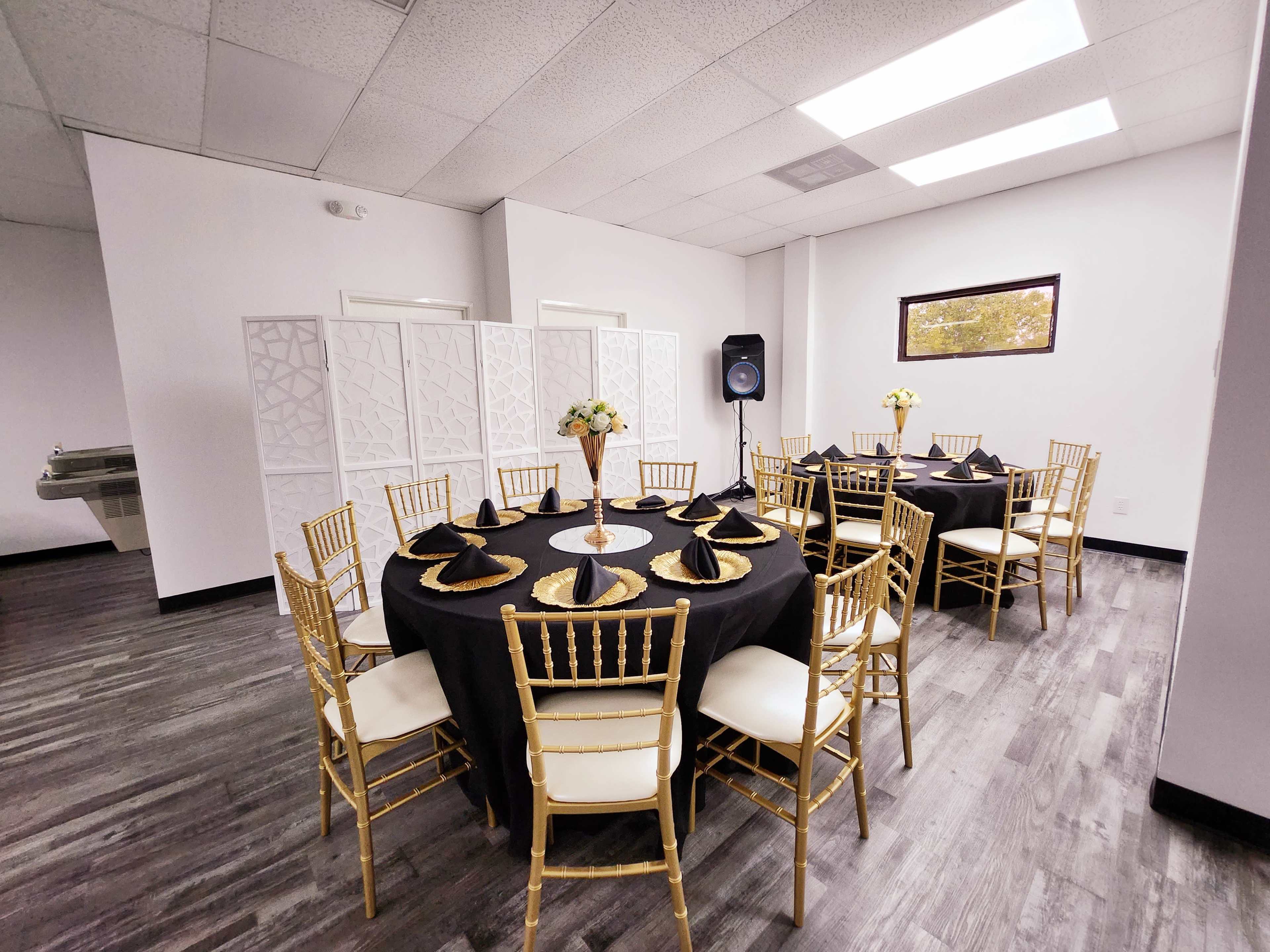 A dining setup with gold-accented tables and chairs arranged around a central flower centerpiece in a modern, bright room.