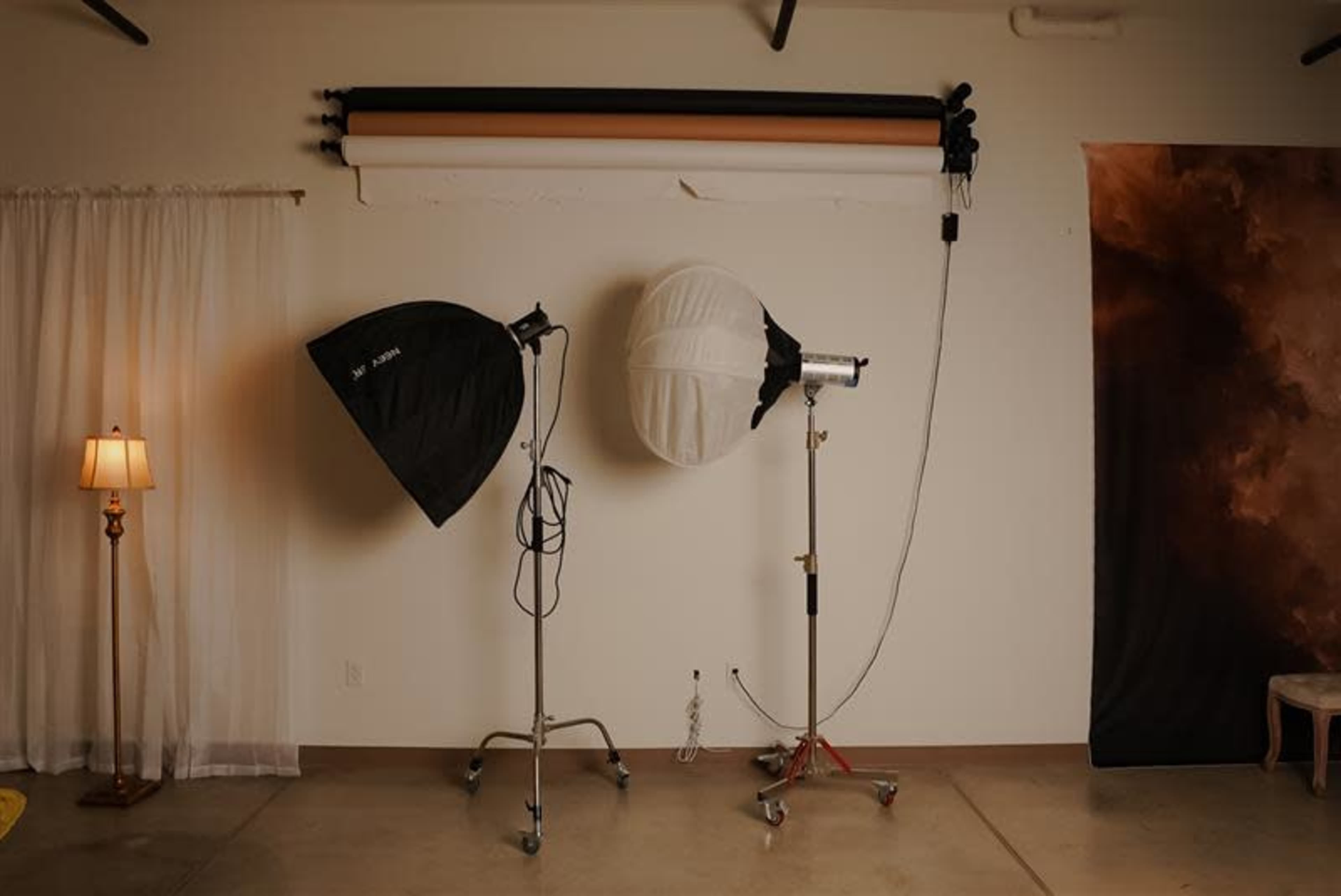 The image shows a photography studio setup with two softboxes on stands and a backdrop with fabric rolls in various colors.