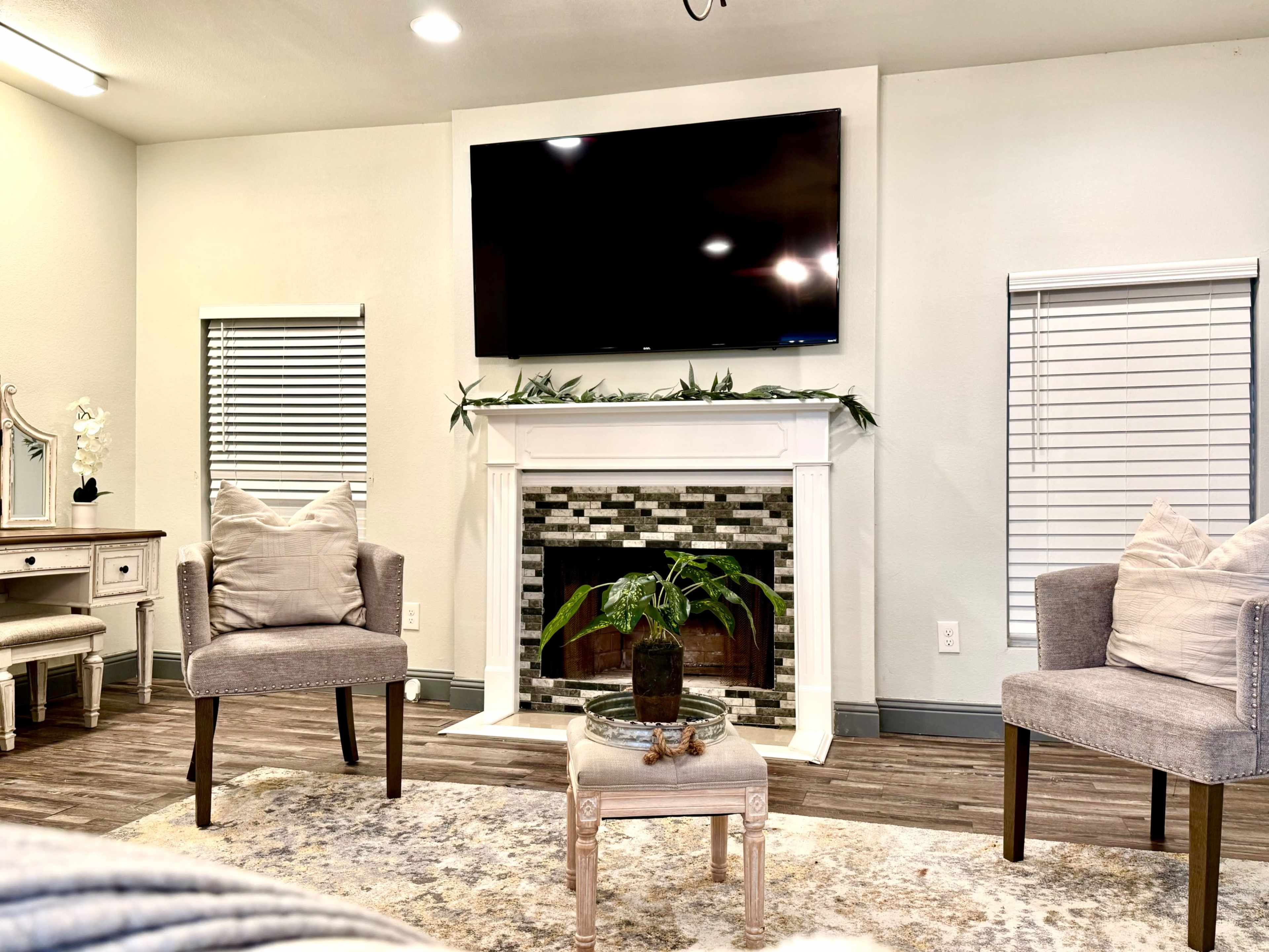 A living room features a modern fireplace with a television mounted above it, flanked by two chairs and a small coffee table.