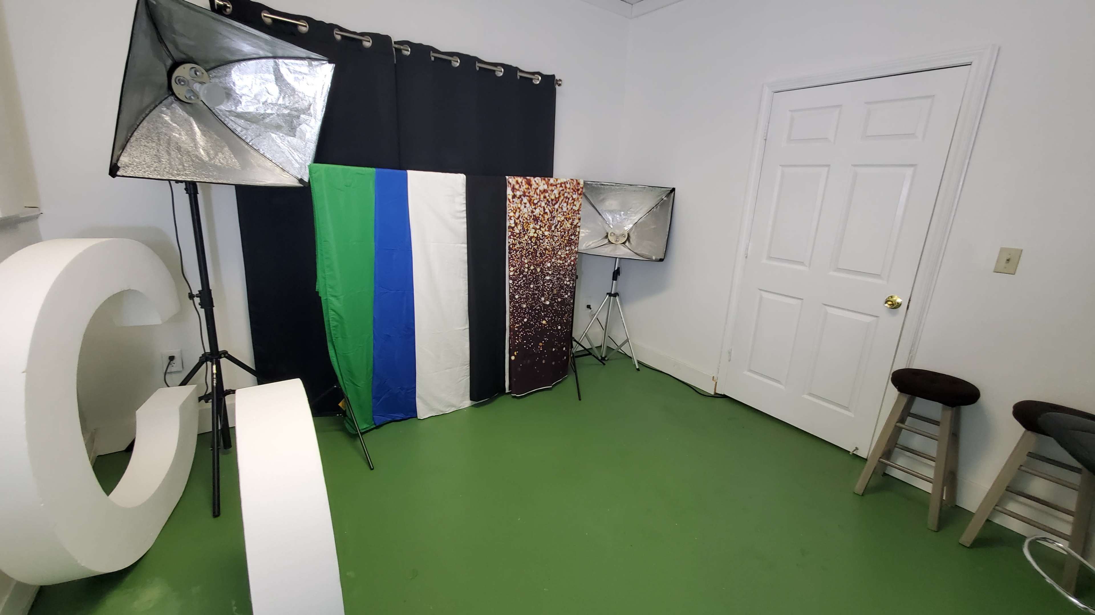 The image shows a small studio space with three backdrop panels and several lighting setups against a wall with a door.
