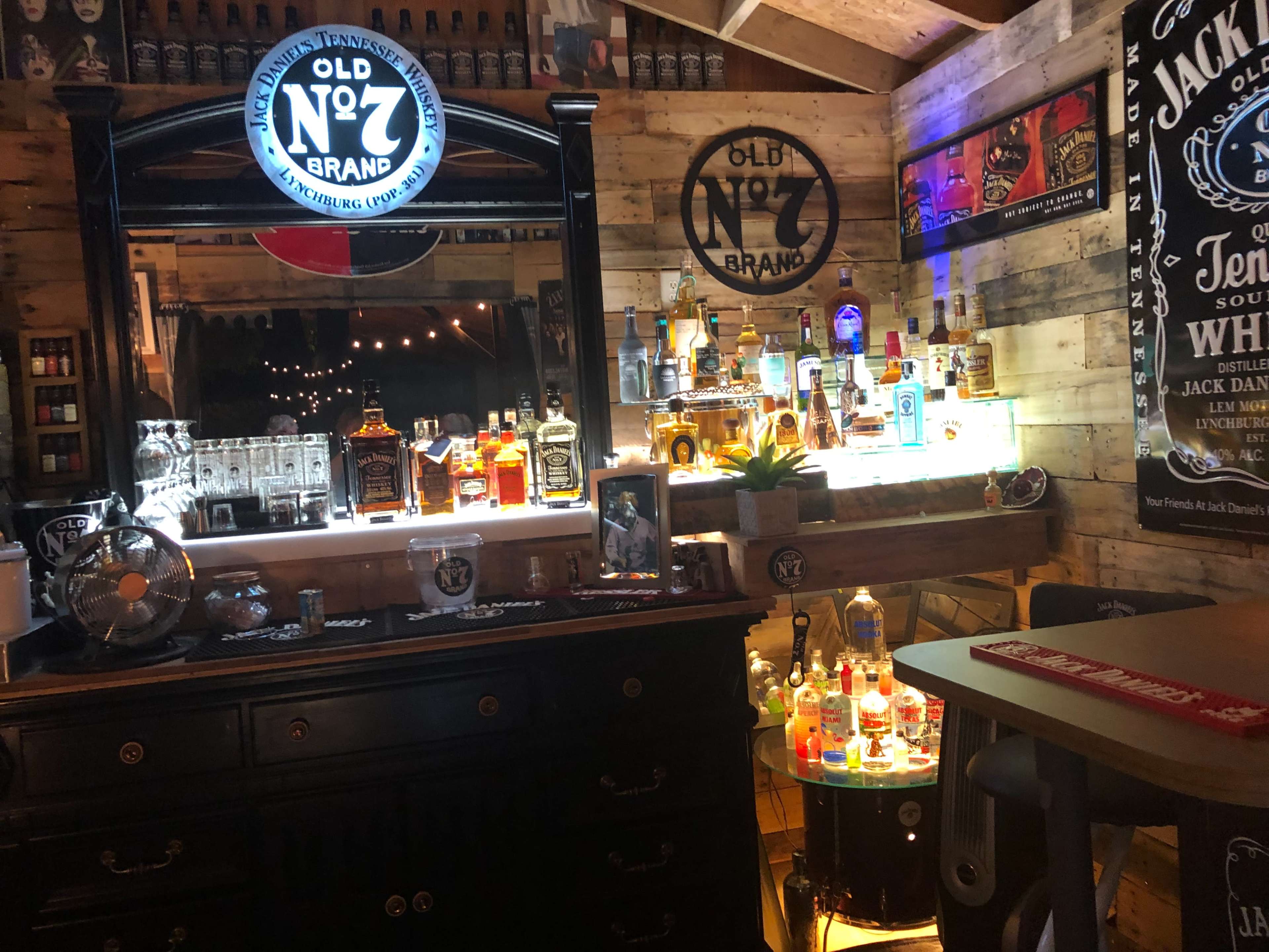 A well-decorated bar area featuring various bottles of liquor displayed on illuminated shelves against a wooden backdrop.