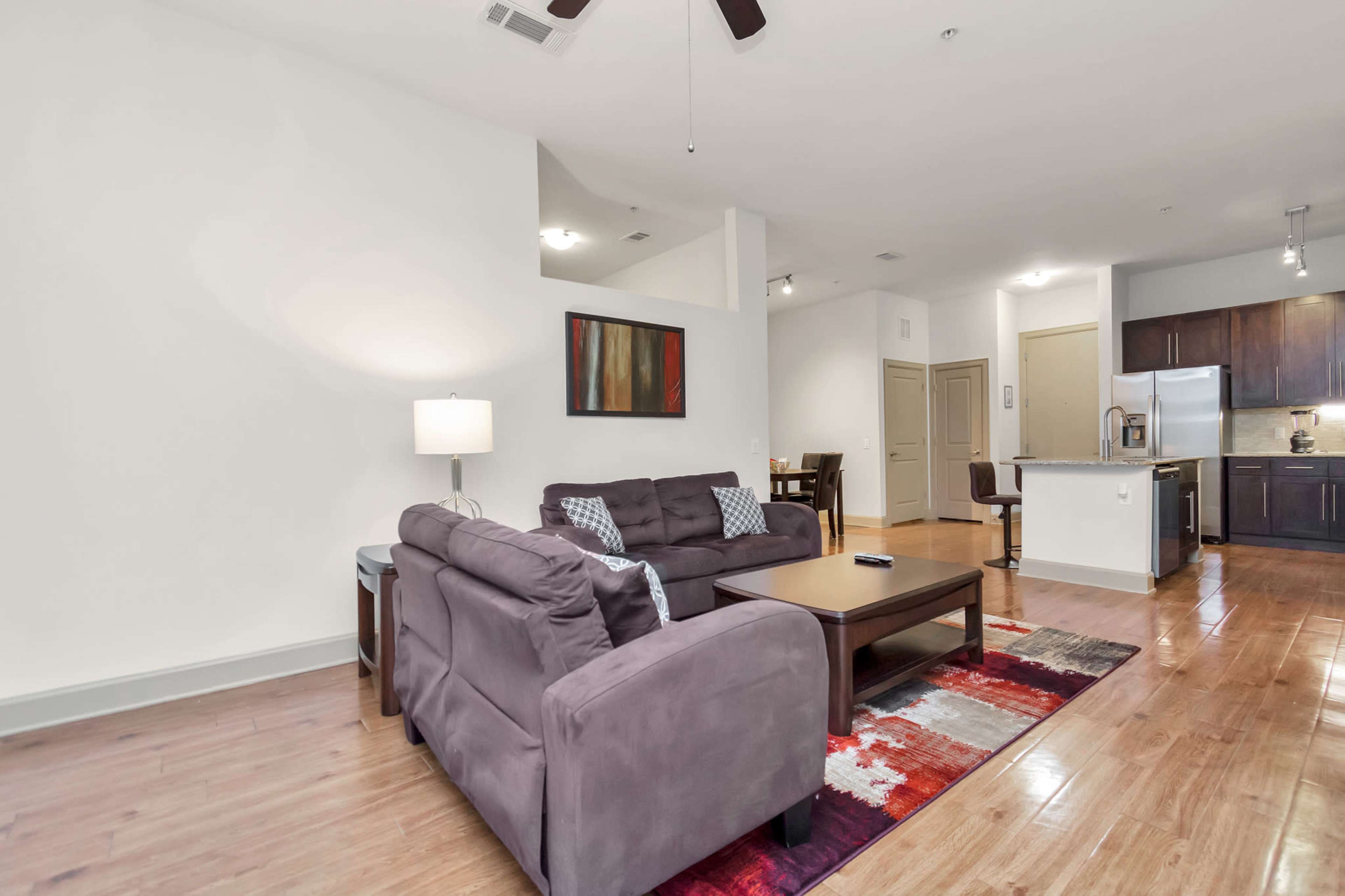 A living room with two couches, a coffee table, and a nearby kitchen area visible in a modern apartment.